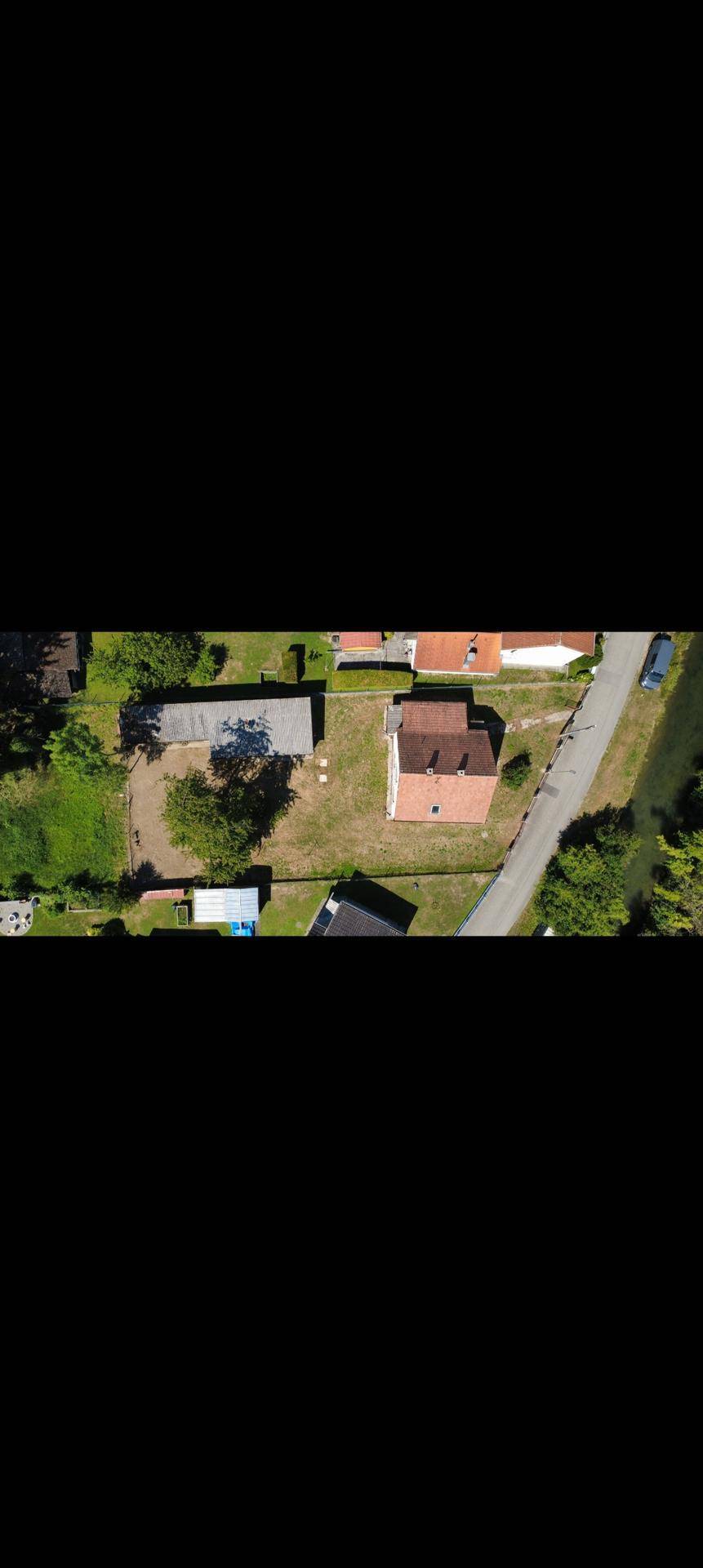 Luftaufnahme eines Grundstücks mit Wohnhaus, Nebengebäude und umliegender Grünfläche.