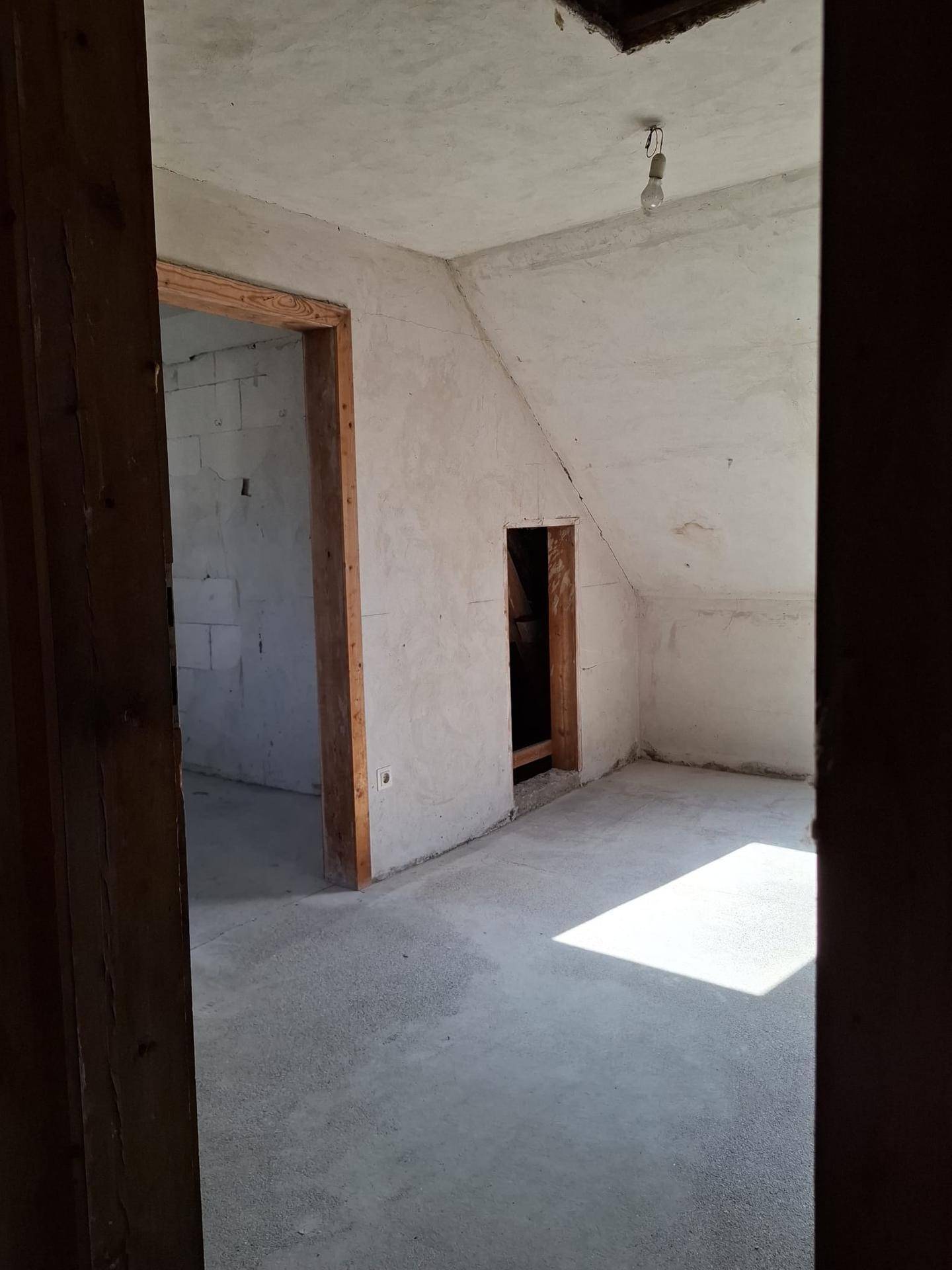 Unfertiger Dachbodenraum mit schrägen Wänden und Betonboden, bereit für den Ausbau.