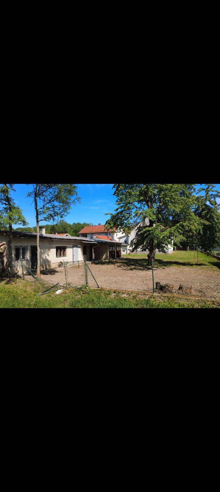 Ansicht eines Nebengebäudes mit einfacher Fassade und umgebendem Grün, möglicherweise eine Garage oder Werkstatt.