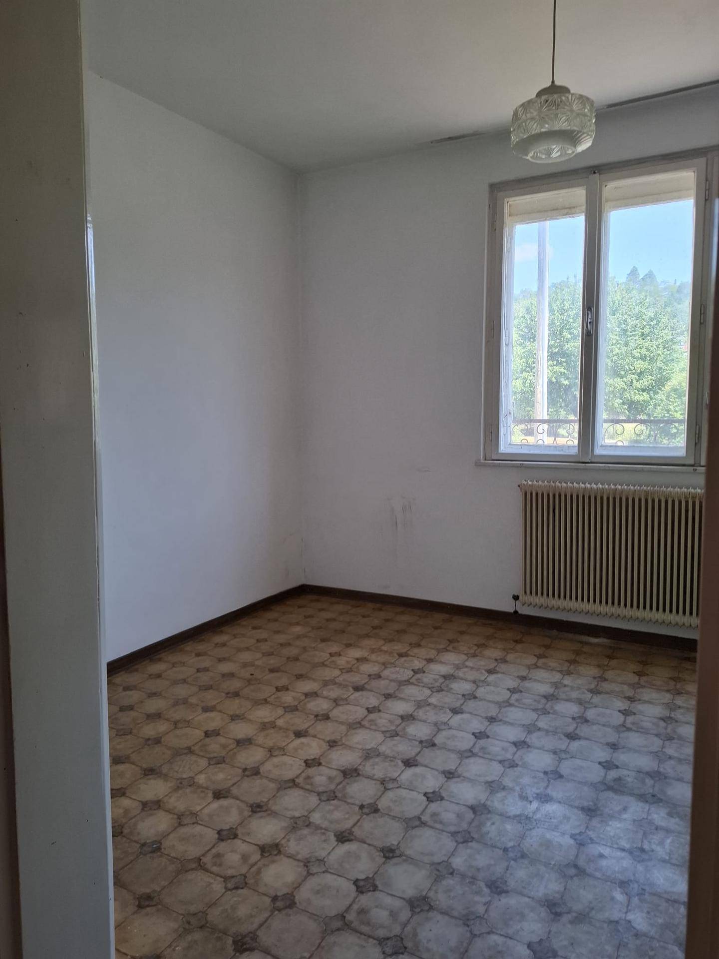 Leerer Raum mit Fenster, Heizkörper und altem gemusterten Boden, der eine Renovierung benötigt.