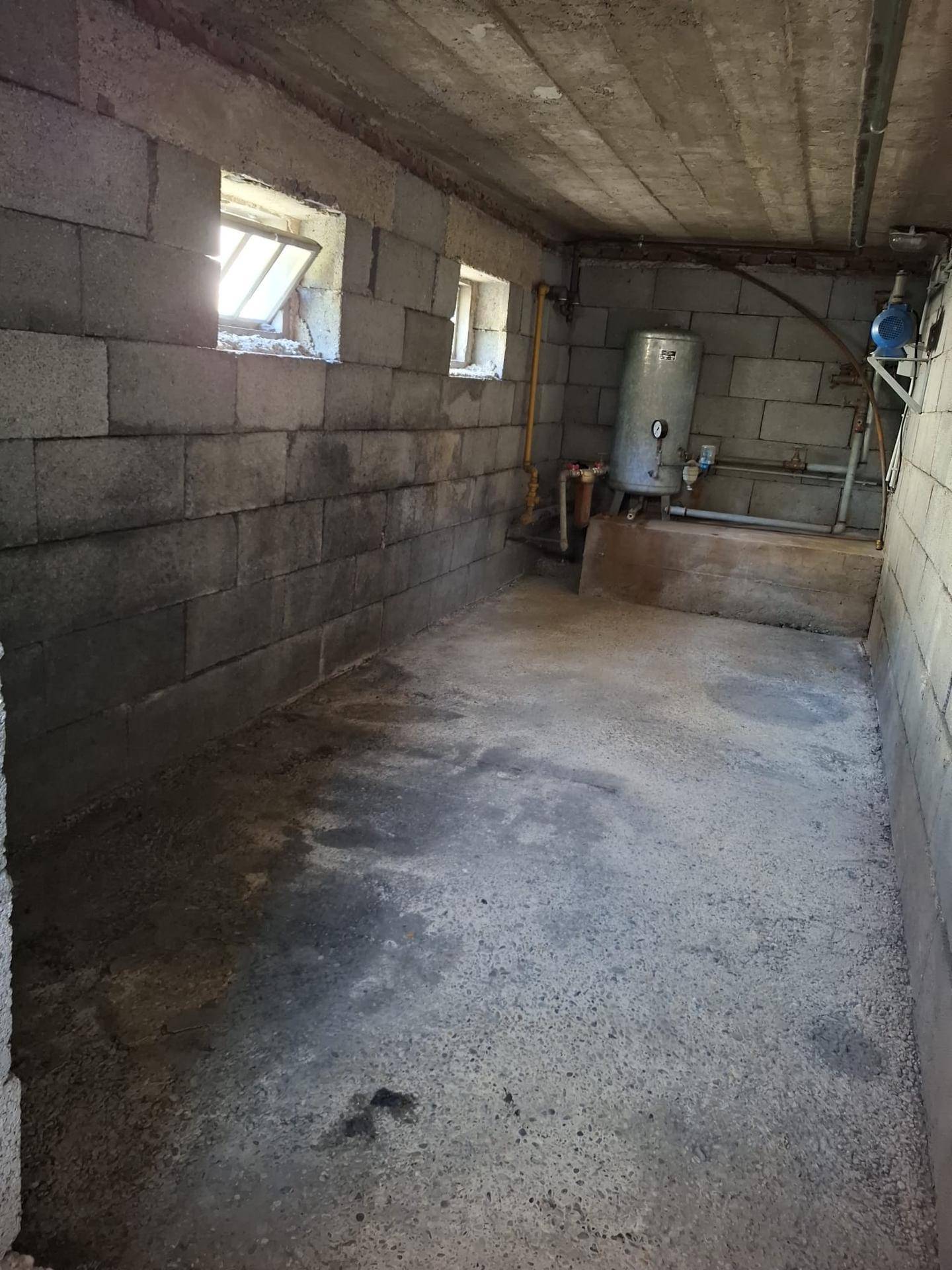 Kellerraum mit Betonwänden, Zementboden und einem Warmwasserboiler, ideal als Lagerfläche.