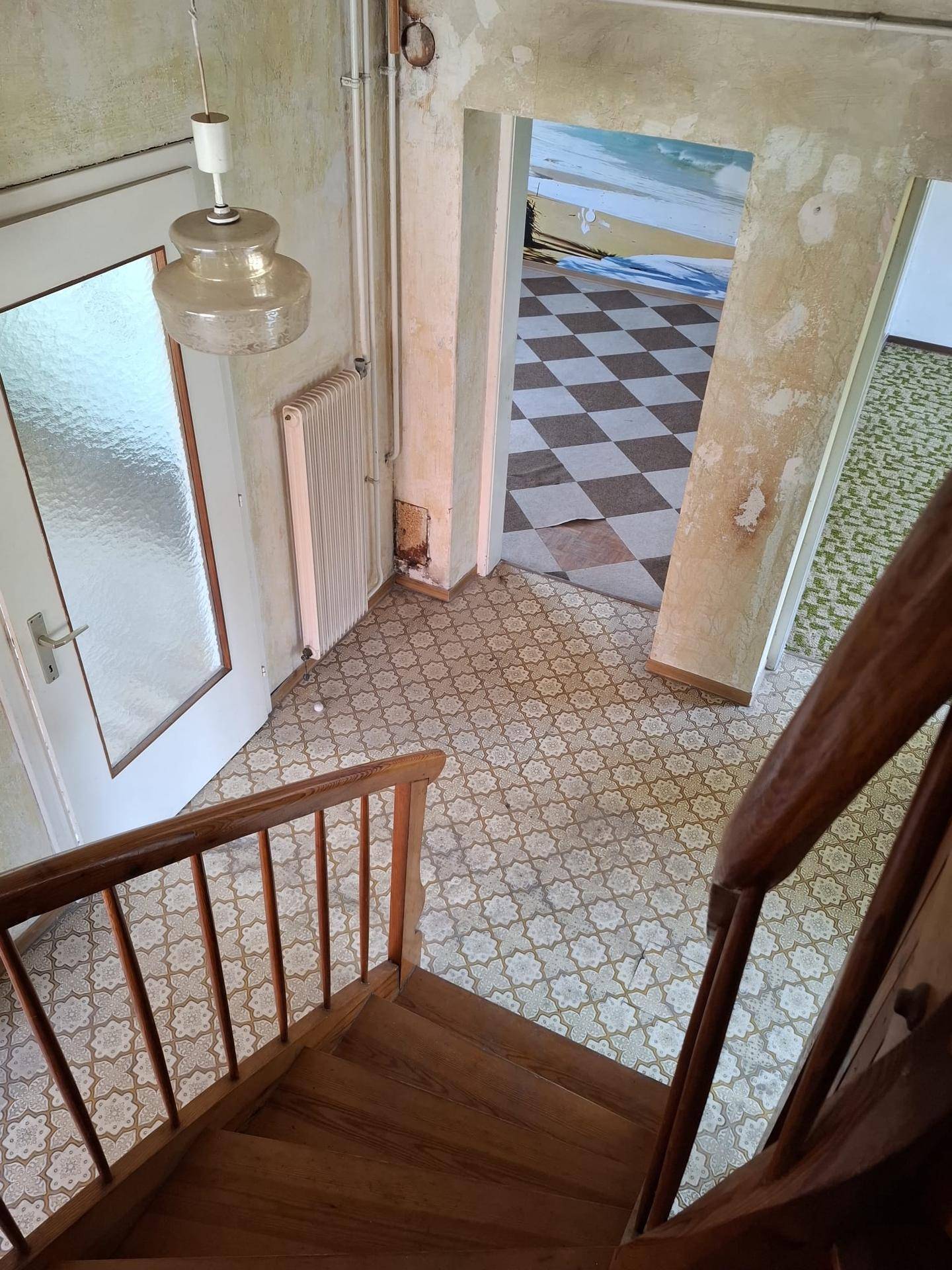 Blick von der Holztreppe in einen Flur mit gemusterten Bodenfliesen und Zugang zu weiteren Räumen.