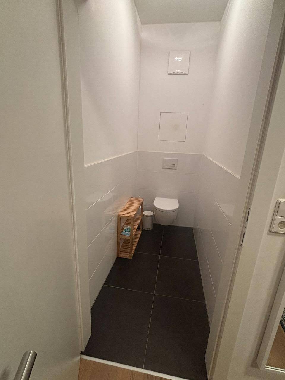 Kleines Gäste-WC mit wandhängendem WC und dunklem Fliesenboden.