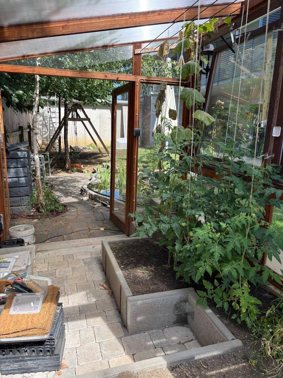 Innenansicht eines Gewächshauses mit wachsenden Pflanzen und Blick in den Garten.