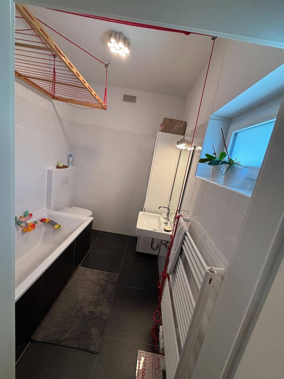 Helles Badezimmer mit Badewanne, Waschbecken, WC und Fenster.