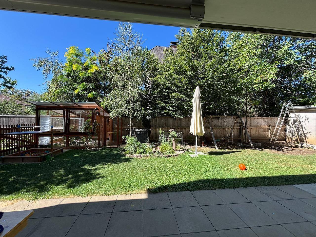 Überdachte Terrasse mit Blick auf den gepflegten Rasen und die Bäume im Garten.