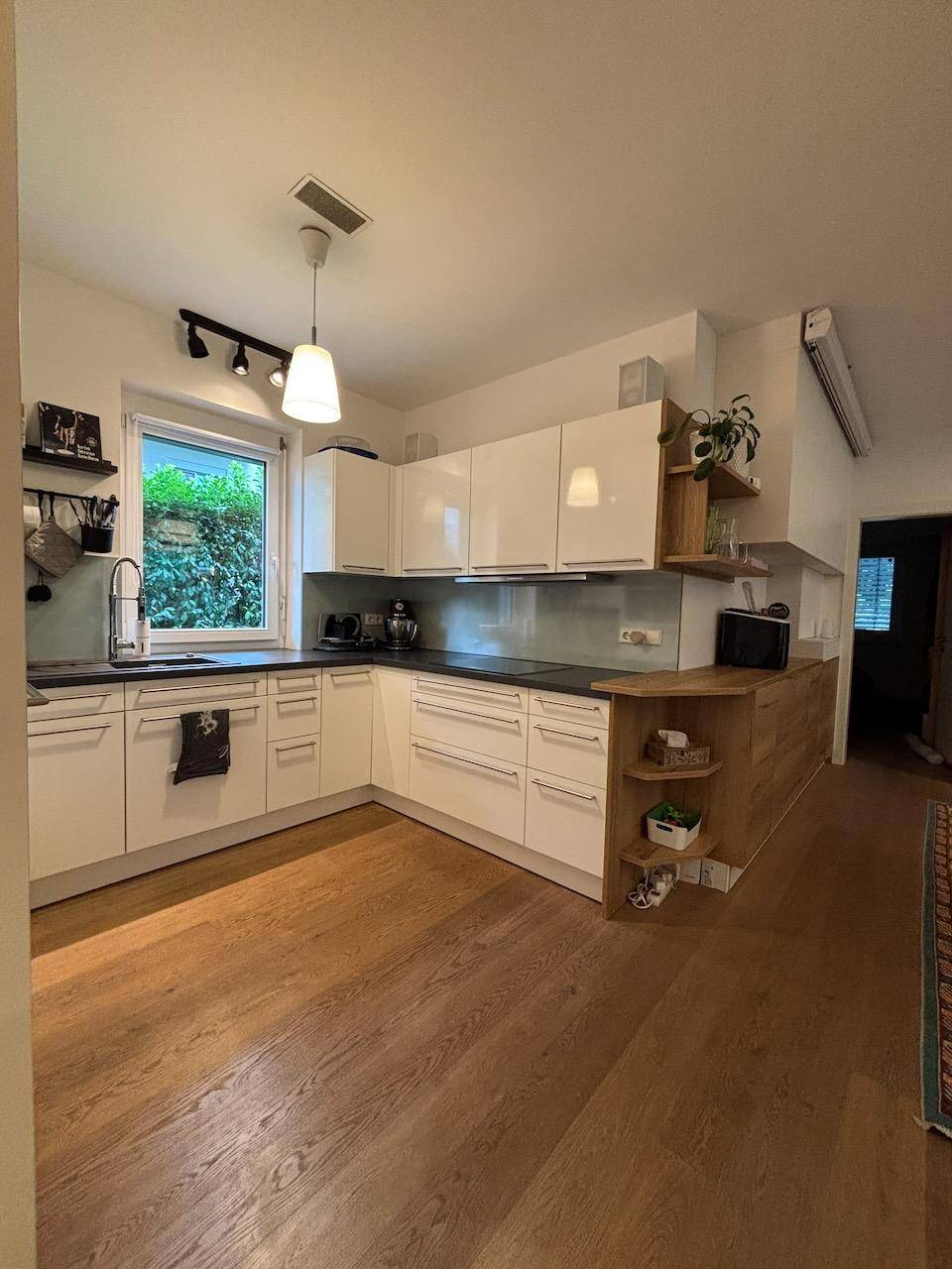 Helle, moderne Küche mit weißen Schränken, Holzdetails und Fenster zum Garten.