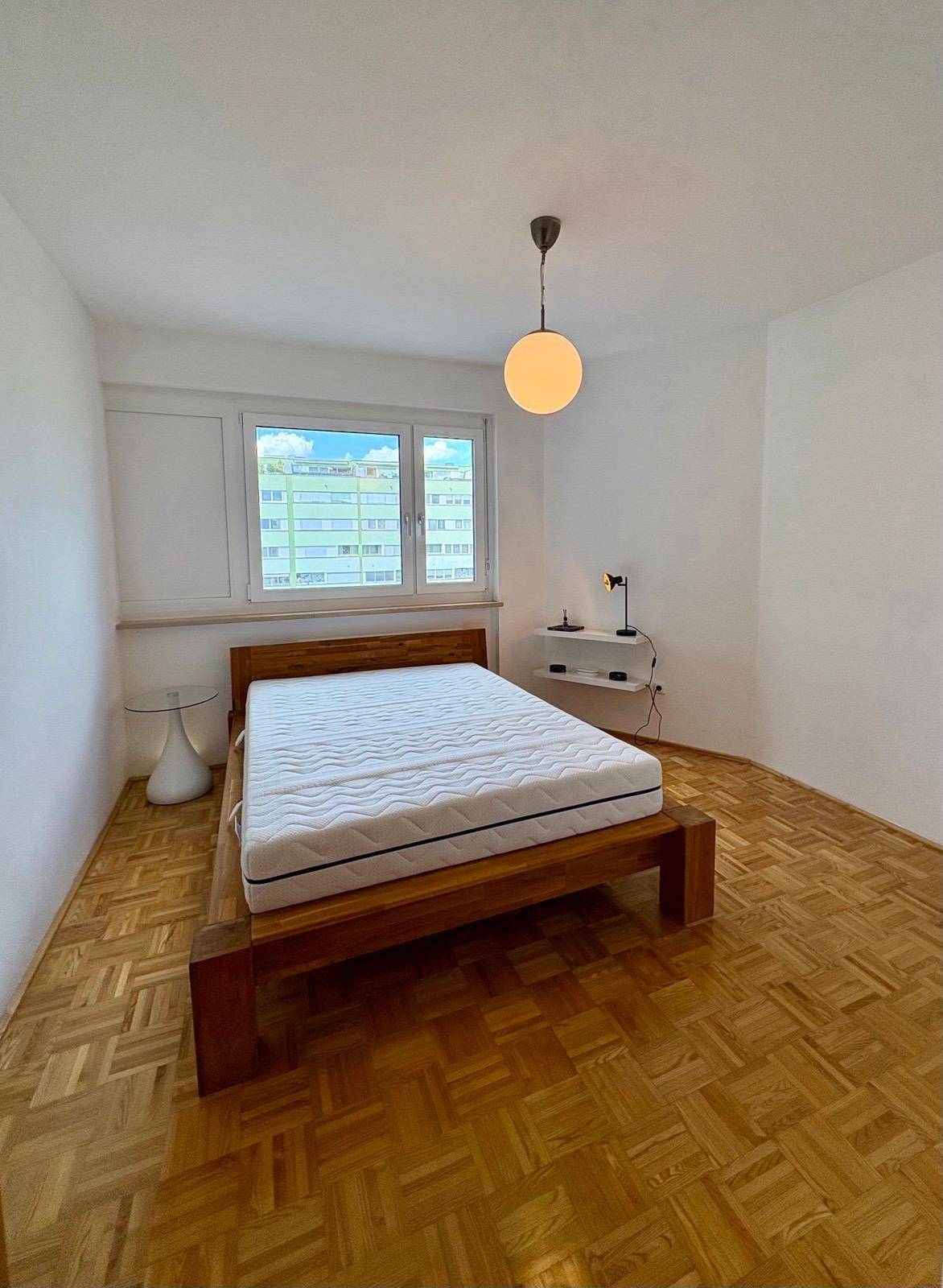 Helles Schlafzimmer mit Holzbett, Parkettboden und großem Fenster.