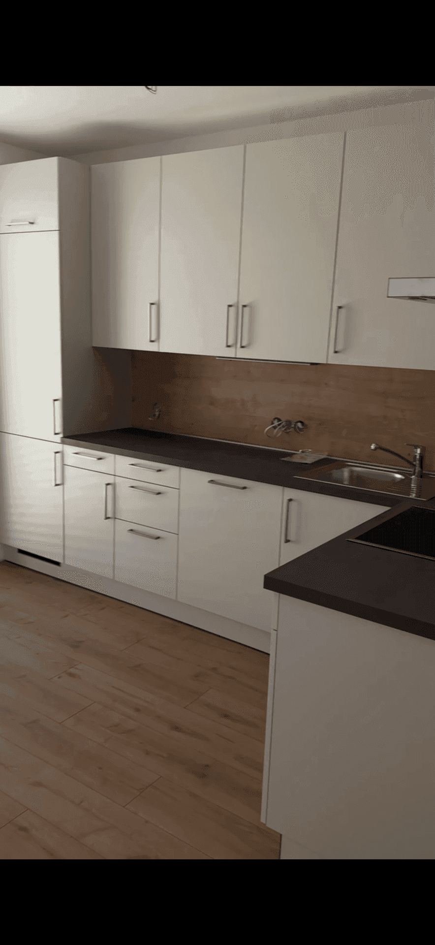Moderne Einbauküche mit weißen Schränken, dunkler Arbeitsplatte und Holzrückwand.