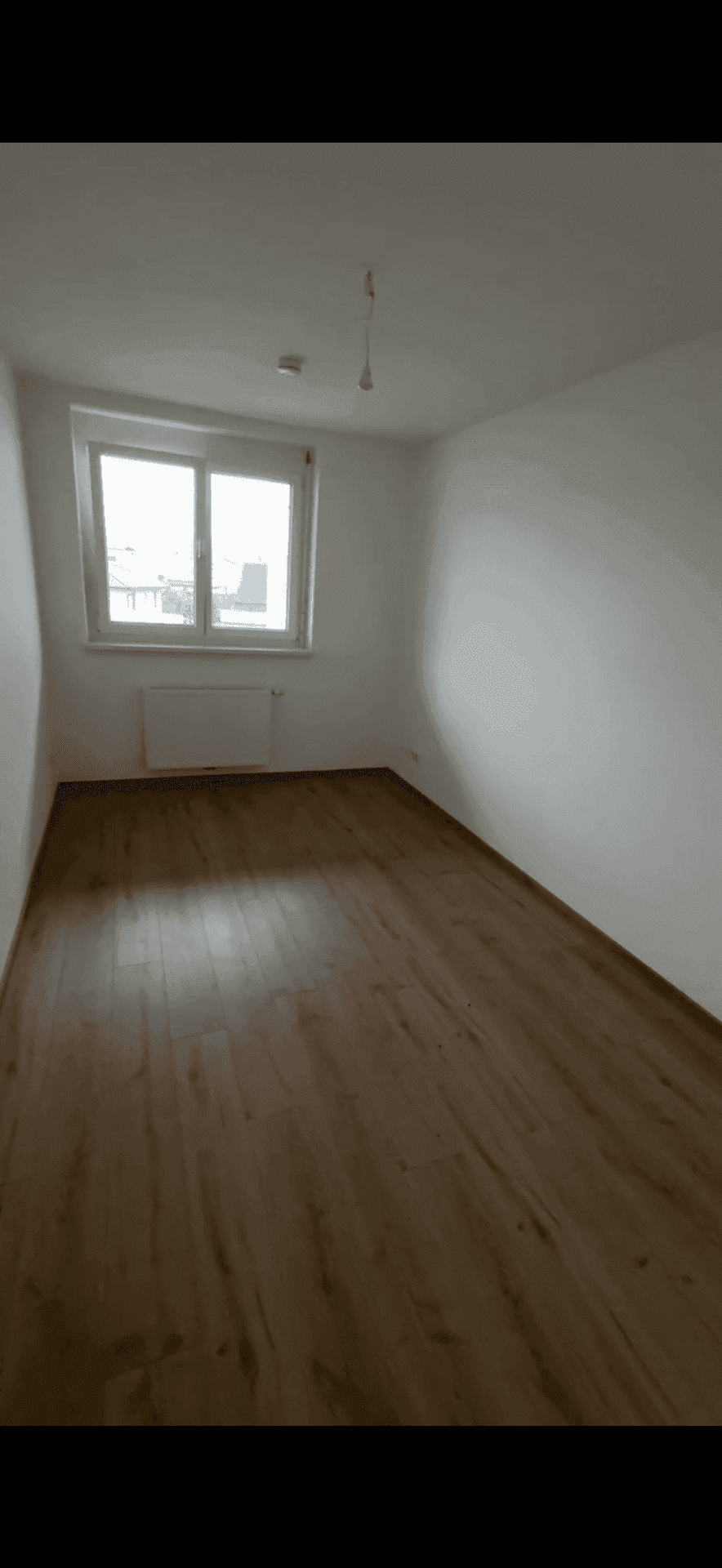 Helles Schlafzimmer mit Laminatboden und einem Fenster, das viel Tageslicht hereinlässt.