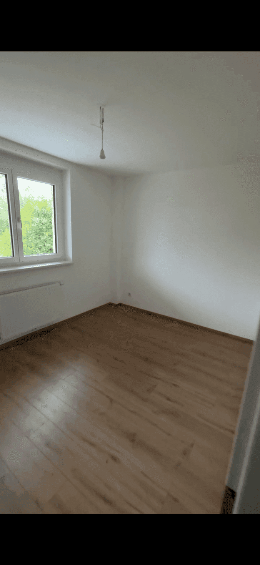 Leeres Schlafzimmer mit Laminatboden, weiß gestrichenen Wänden und einem Fenster.