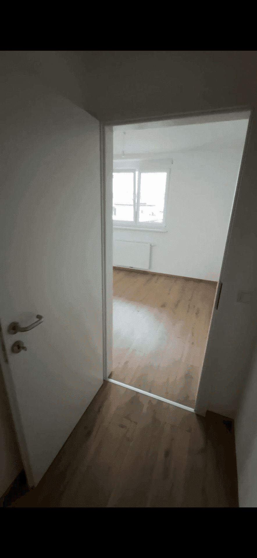 Türöffnung zu einem weiteren Raum mit Laminatboden und weiß gestrichenen Wänden.