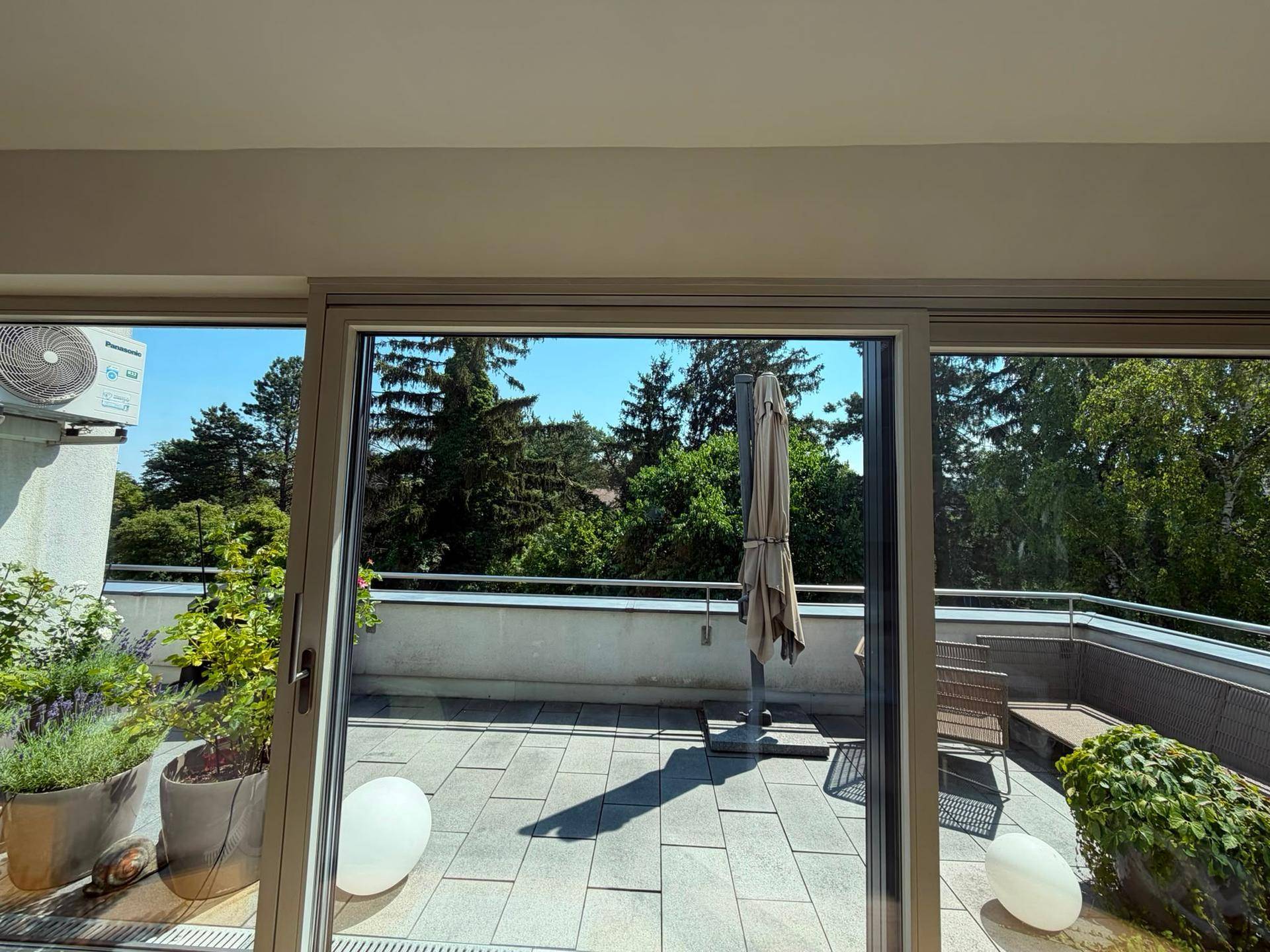 Heller Innenraum mit großen Schiebetüren, die auf eine geräumige Terrasse mit viel Grün führen.