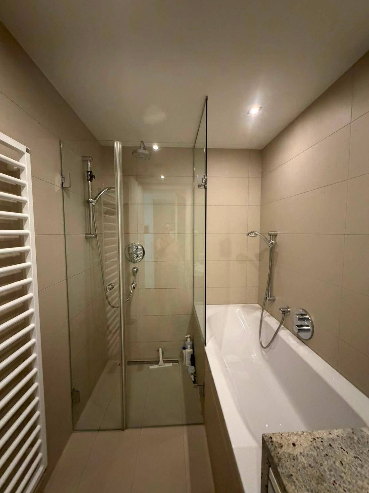 Modernes Badezimmer mit beigen Fliesen, Badewanne, begehbarer Dusche und Handtuchheizkörper.