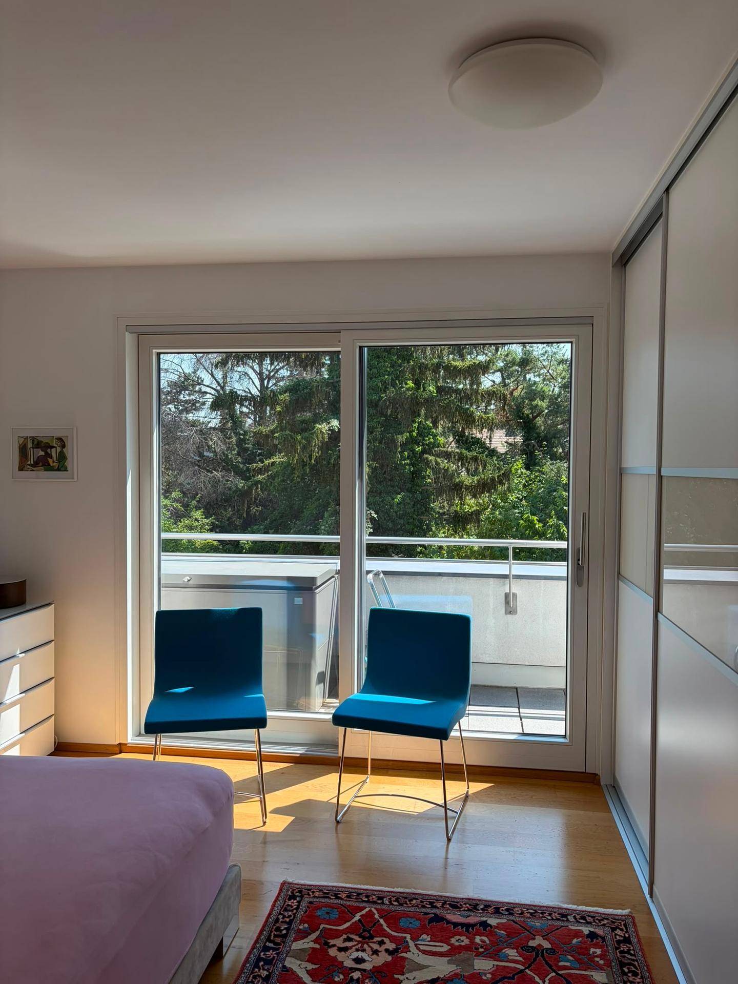 Helles Schlafzimmer mit Holzboden, Schiebetür zum Balkon und einem schönen Blick ins Grüne.
