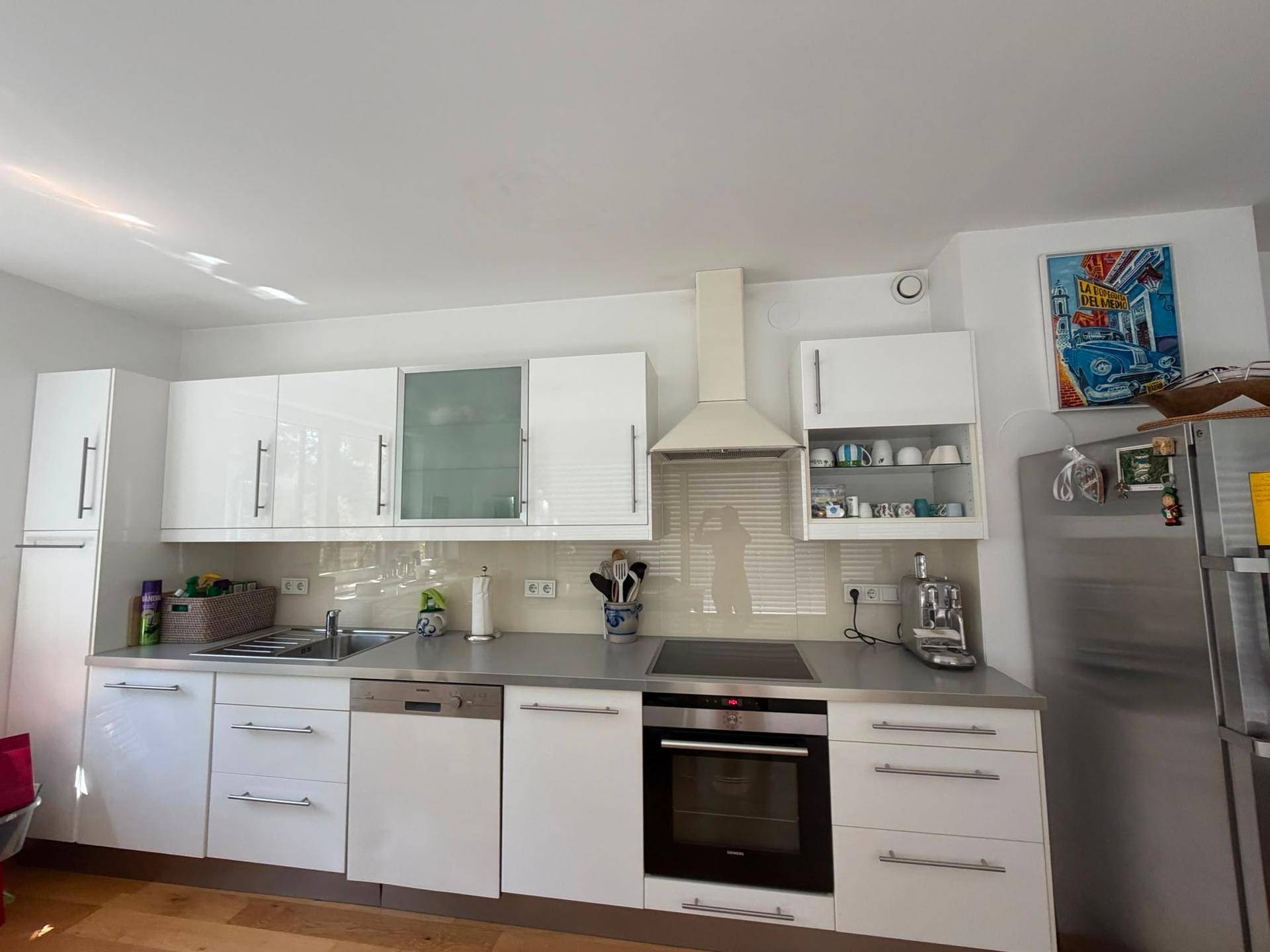 Moderne weiße Einbauküche mit Edelstahlgeräten, Induktionskochfeld und viel Stauraum.
