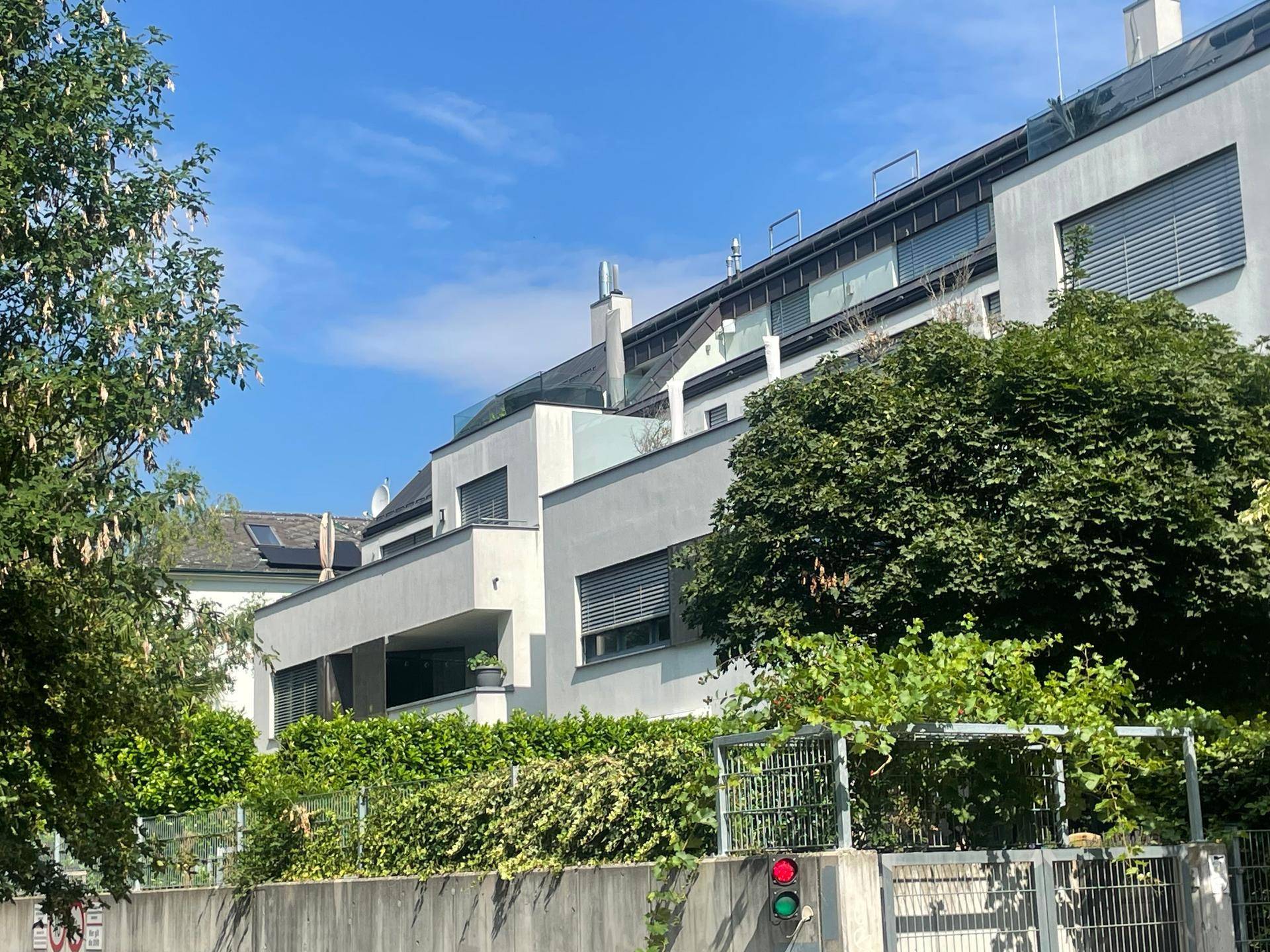 Moderne Architektur mit mehreren Balkonen und grünen Hecken unter strahlend blauem Himmel.