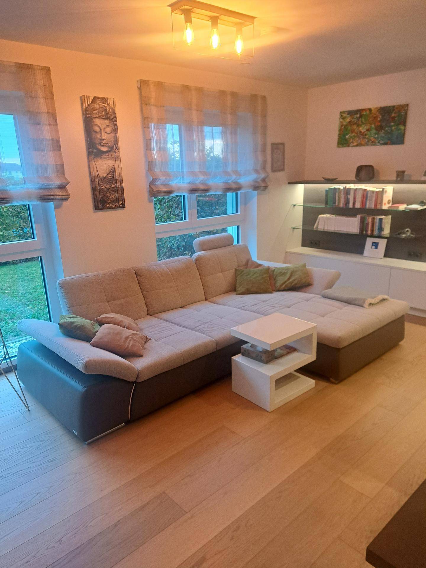 Gemütliches Wohnzimmer mit großem Ecksofa, Holzboden und Blick ins Grüne durch die Fenster.