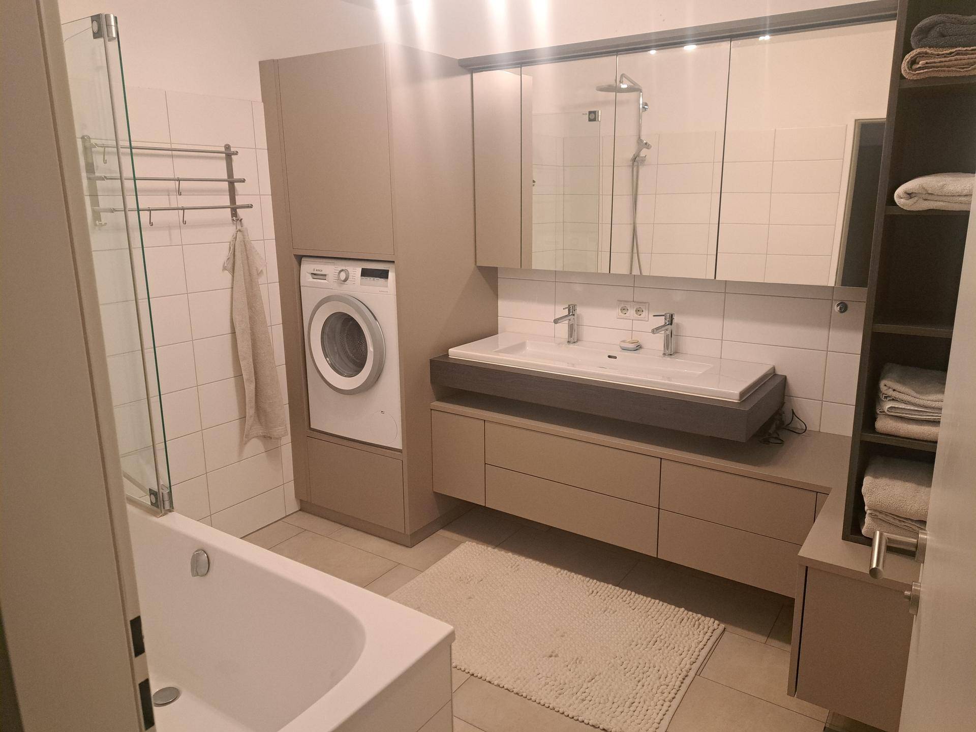 Modernes Badezimmer mit Doppelwaschbecken, Badewanne, Dusche und integrierter Waschmaschine.