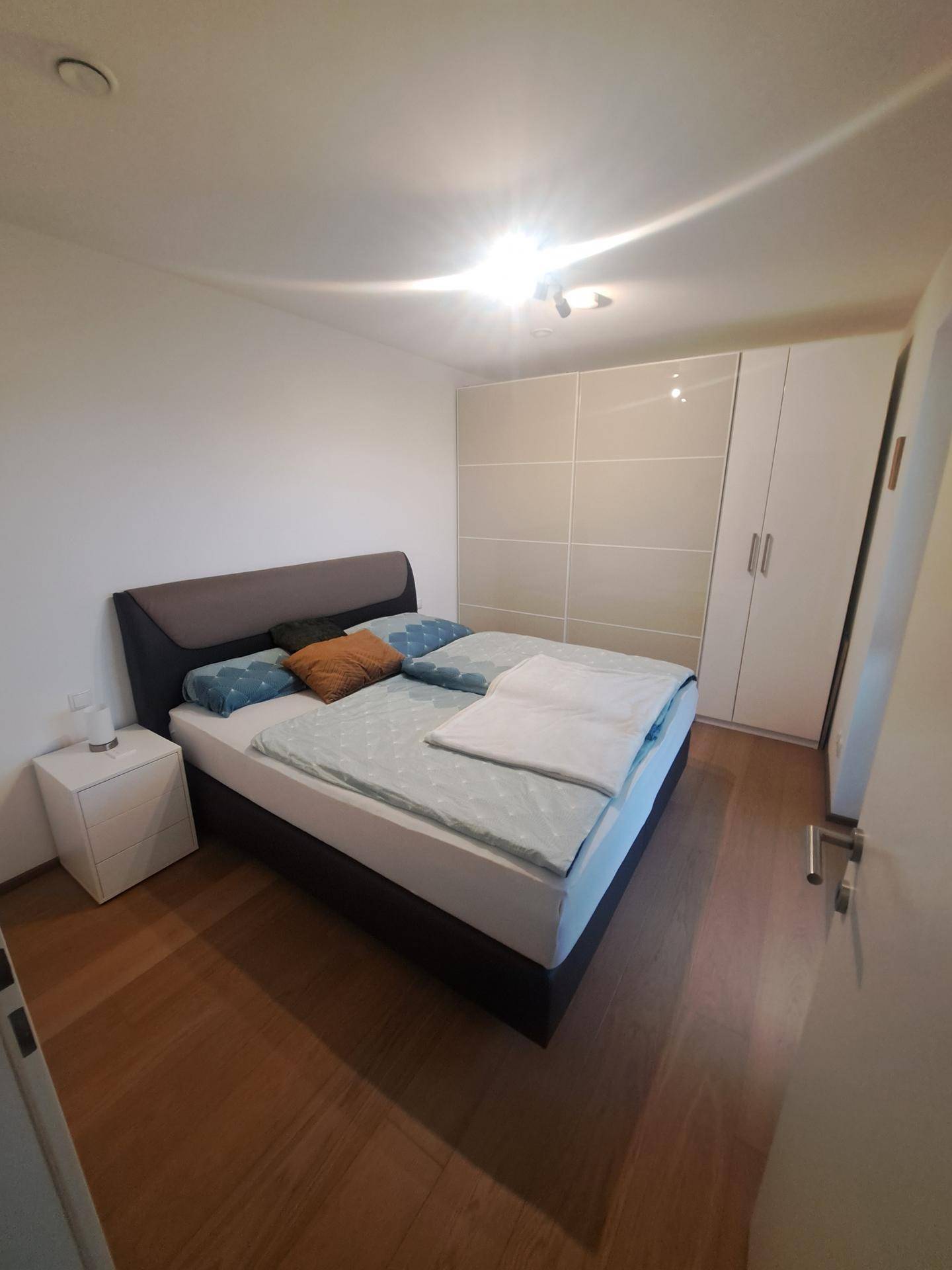 Schlafzimmer mit Doppelbett, Holzboden und großem Kleiderschrank in hellem Design.