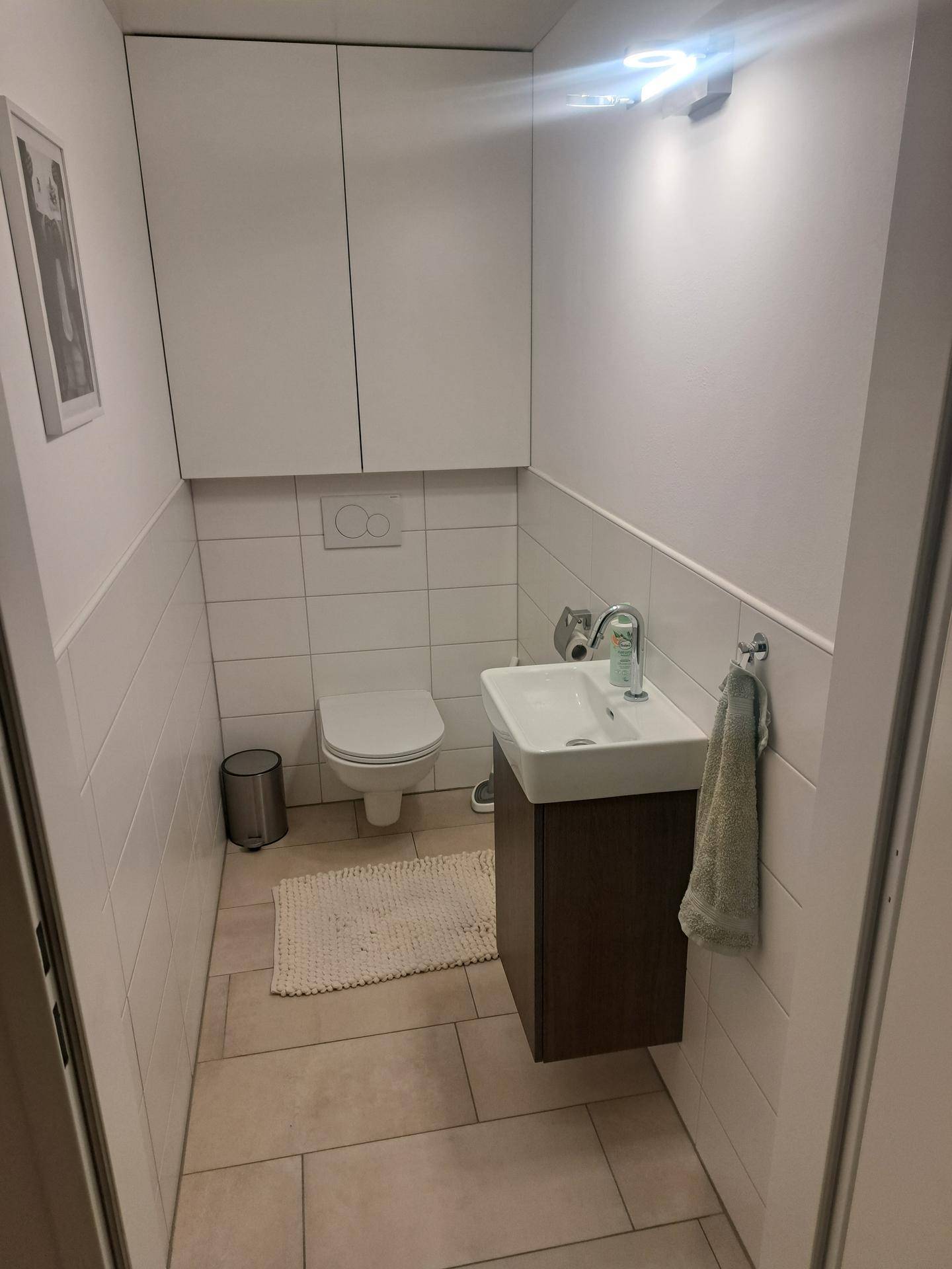 Kleines Gäste-WC mit Wand-WC, Waschbecken und hellen Fliesen an den Wänden.