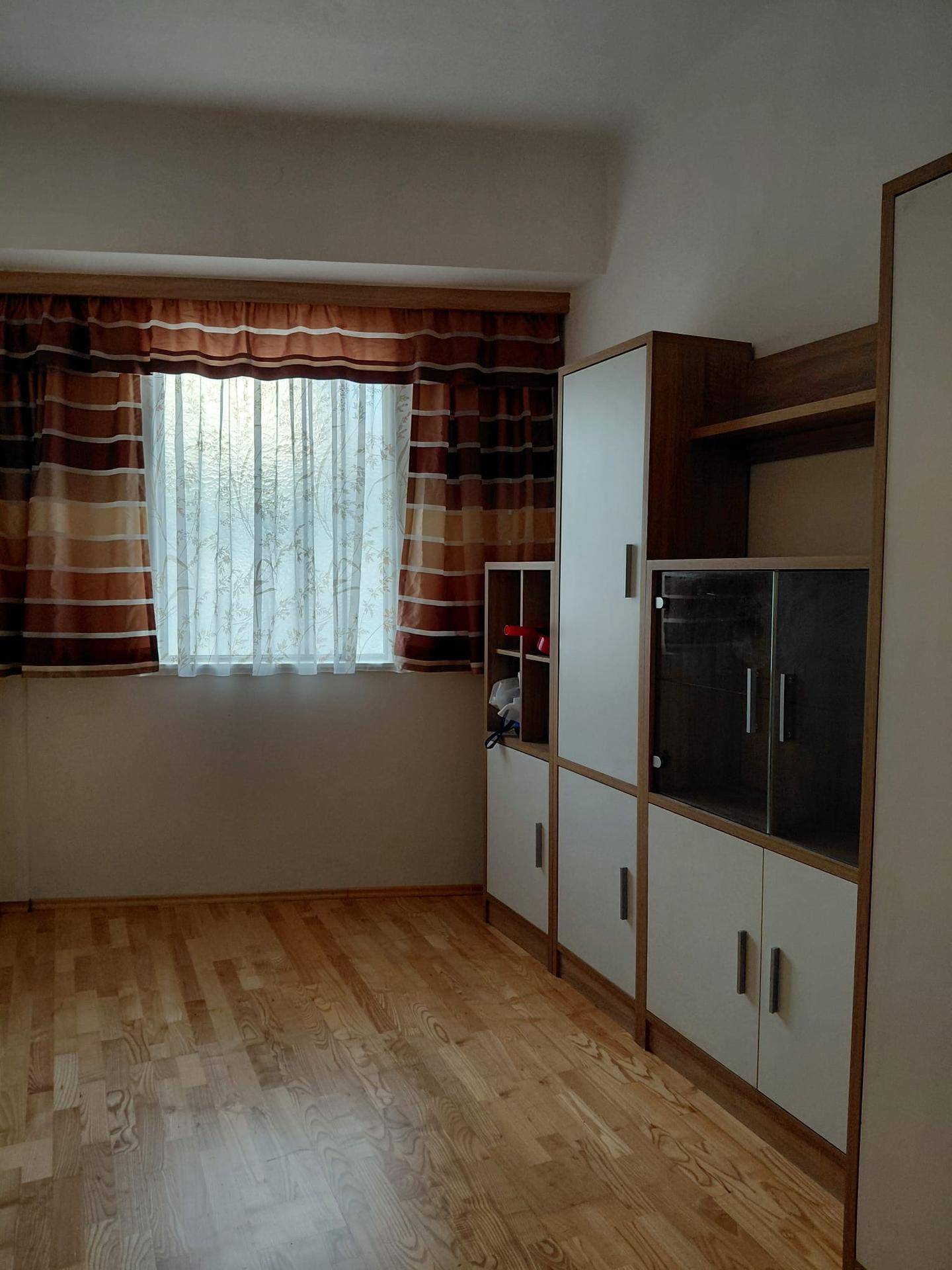 Schlafzimmer mit Parkettboden, Fenster und einem praktischen Wandschrank mit Ablageflächen.
