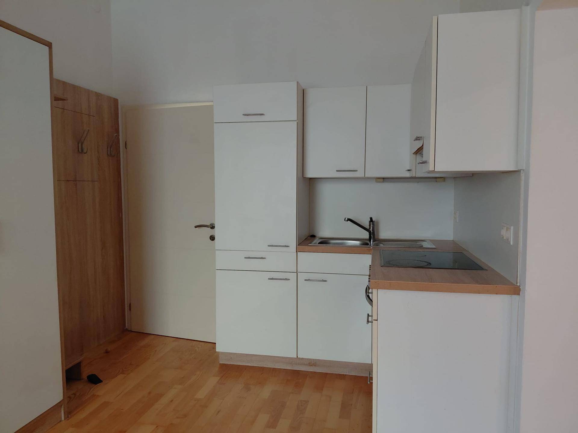Funktionale Küchenzeile mit weißen Schränken, Holz-Arbeitsplatte und Kochfeld in hellem Raum.