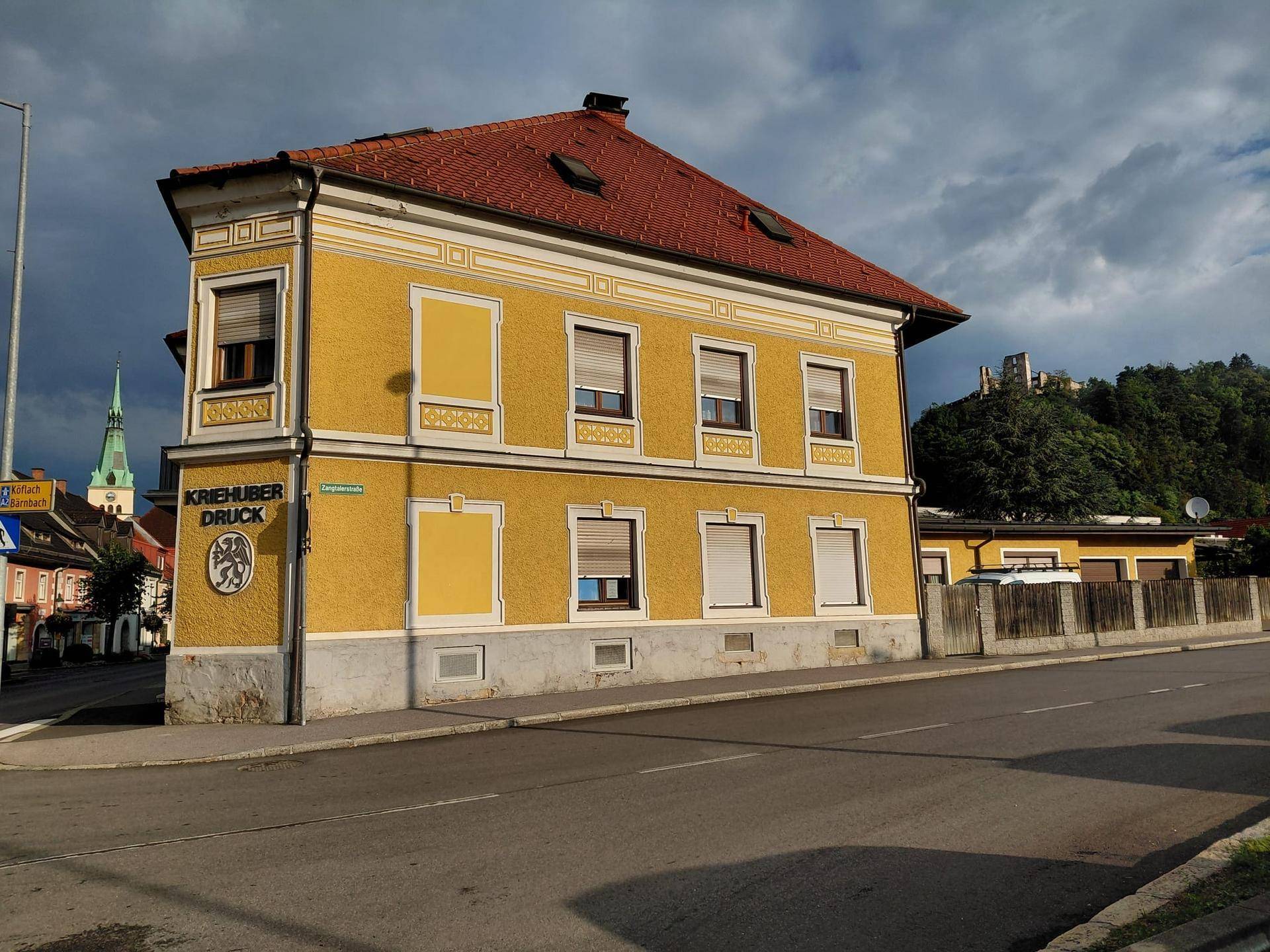 Traditionelles Gebäude mit gelber Fassade und rotem Ziegeldach an einer städtischen Straßenecke.