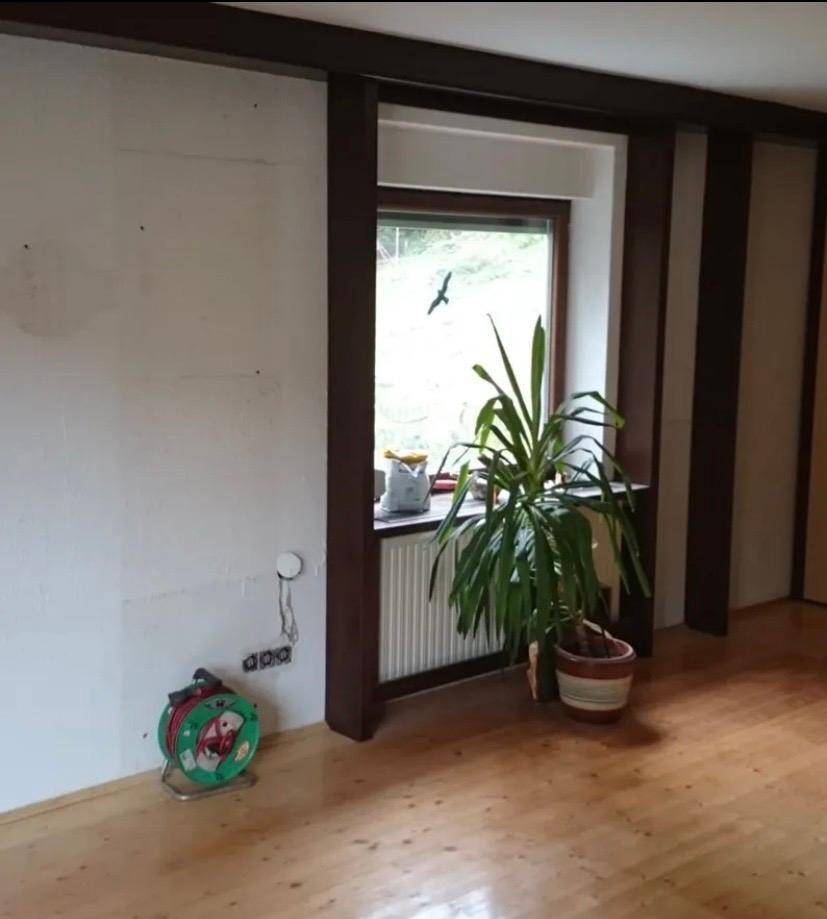 Heller Wohnraum mit Holzfußboden, großem Fenster und Ausblick ins Grüne.