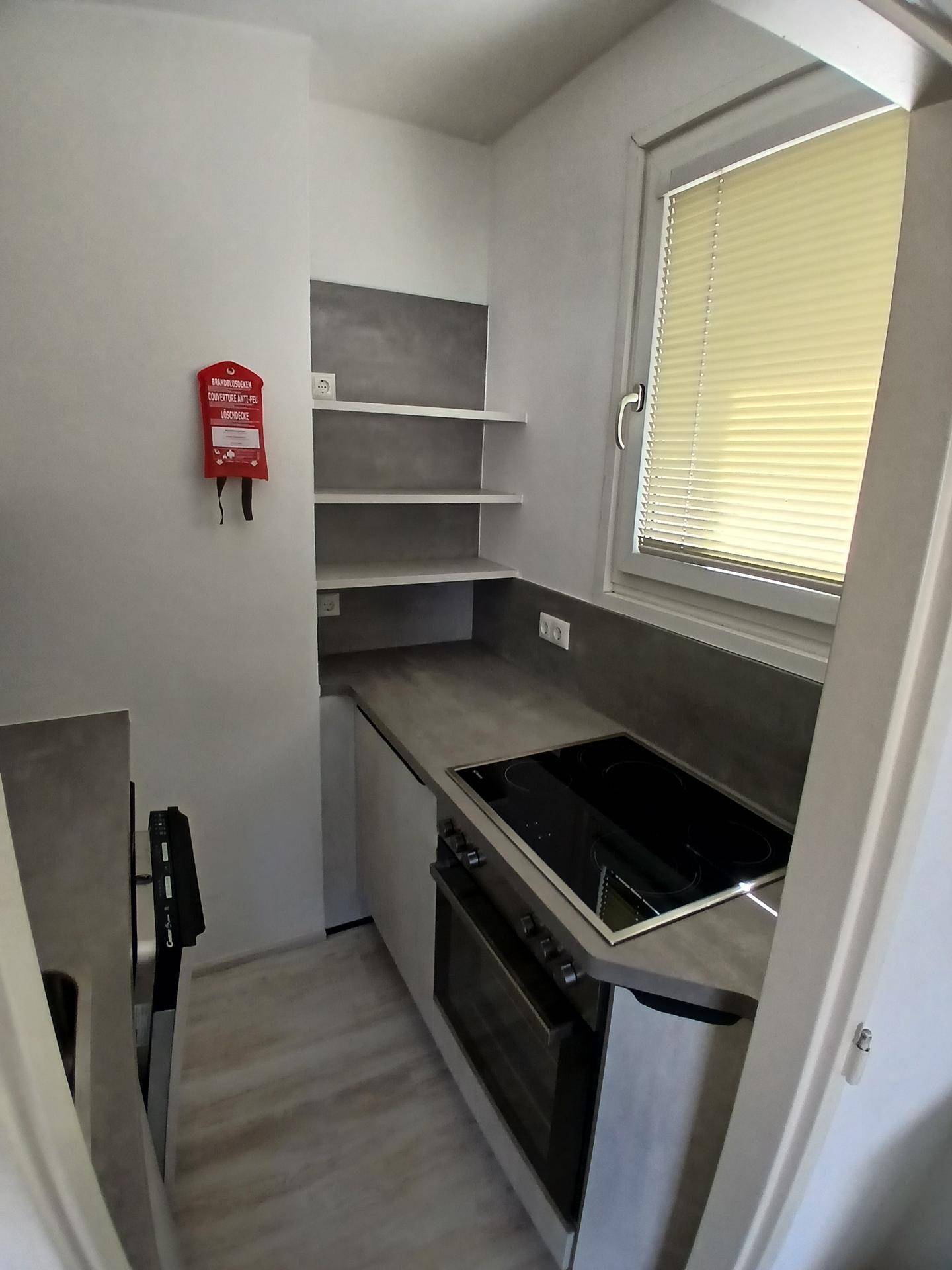 Kompakte Küchenzeile mit Kochfeld, Backofen, Spüle und Fenster für Tageslicht.
