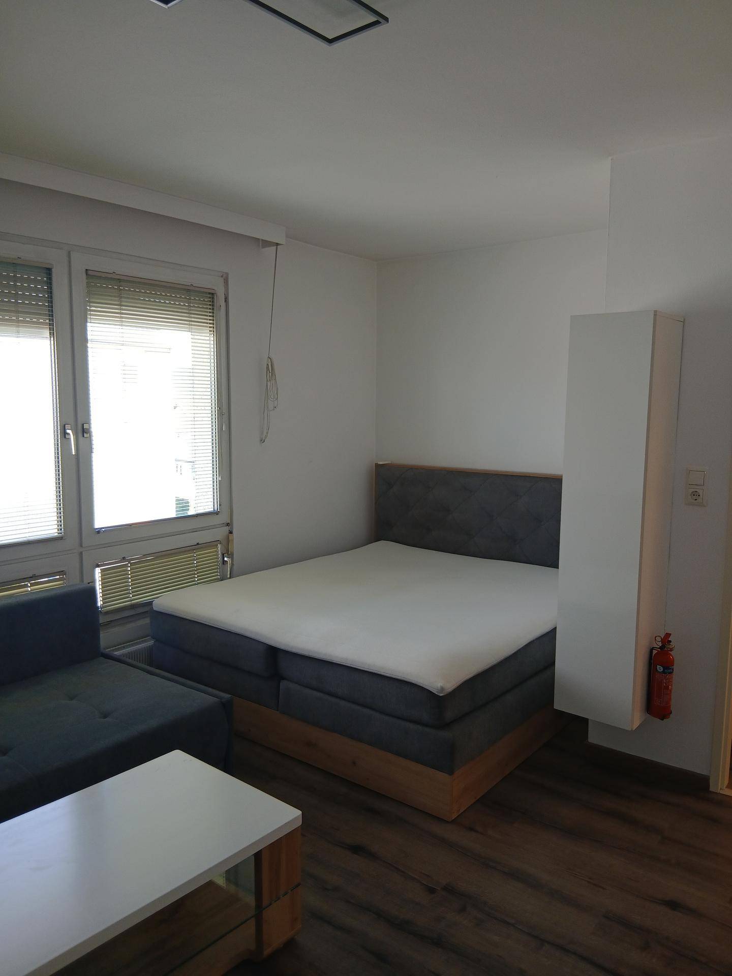 Kombinierter Wohn- und Schlafbereich mit Doppelbett, Sofa und großen Fenstern.