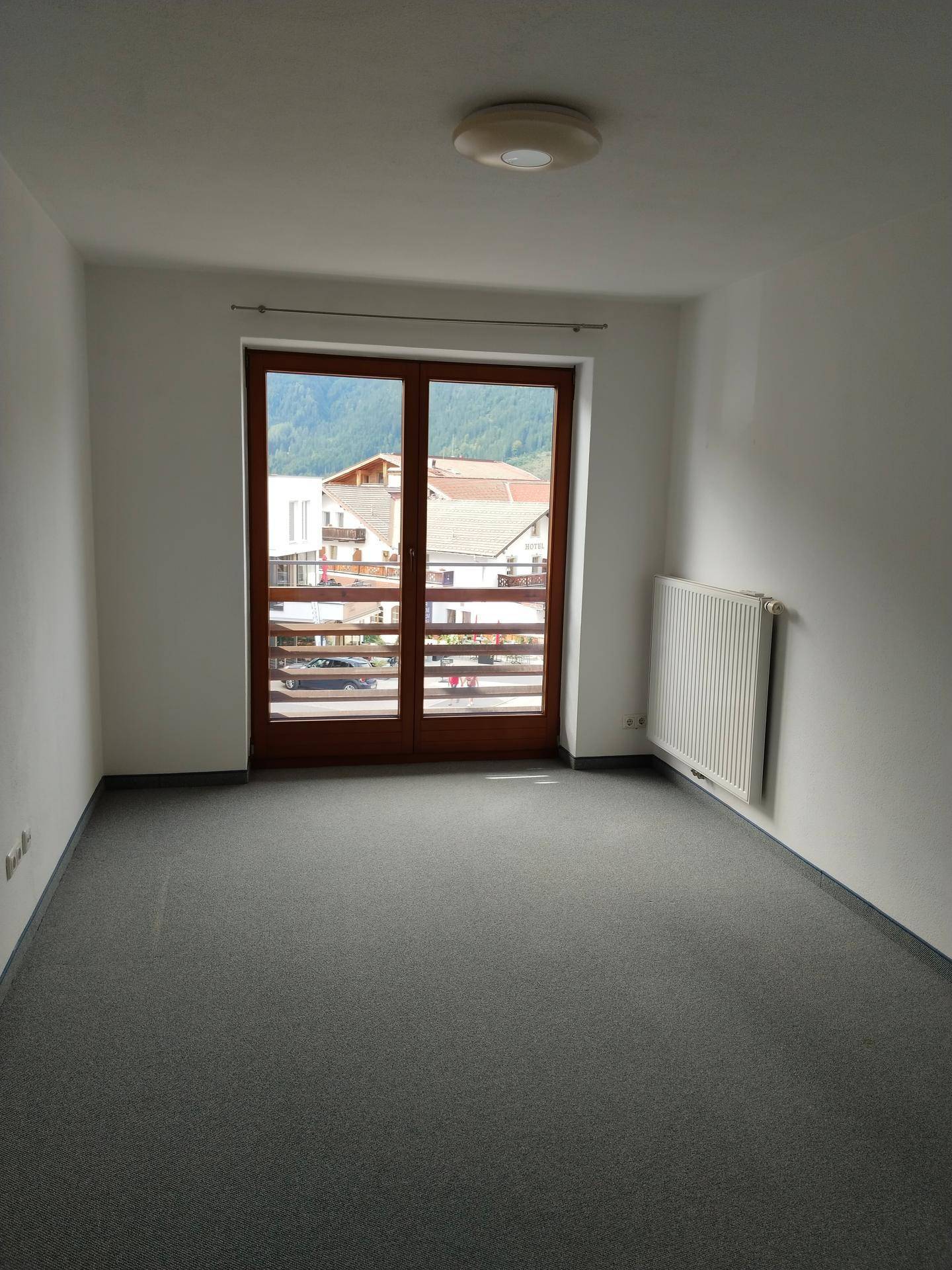 Schlafzimmer mit grauem Teppichboden, Balkonzugang und Blick auf die umliegende Berglandschaft.