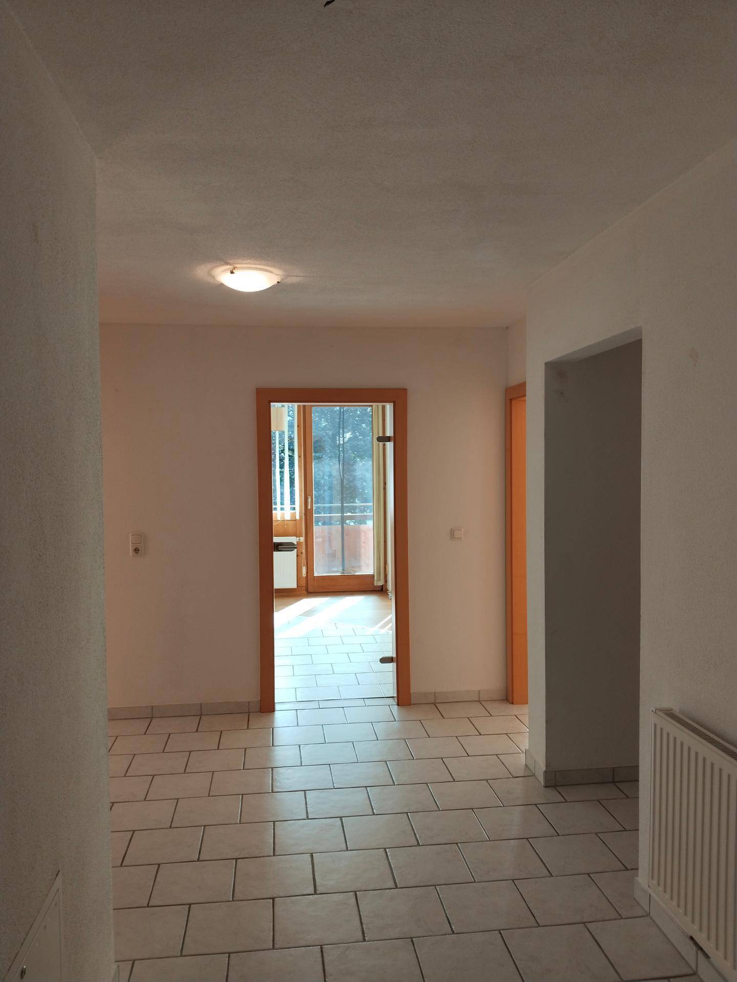 Heller Flur mit Fliesenboden und Zugang zu einem Zimmer mit Balkon.