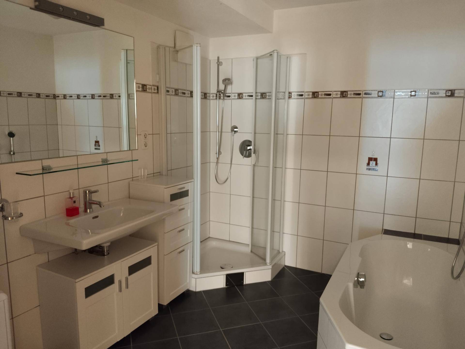 Badezimmer mit weißen Fliesen, Duschkabine, Badewanne und Waschtisch.