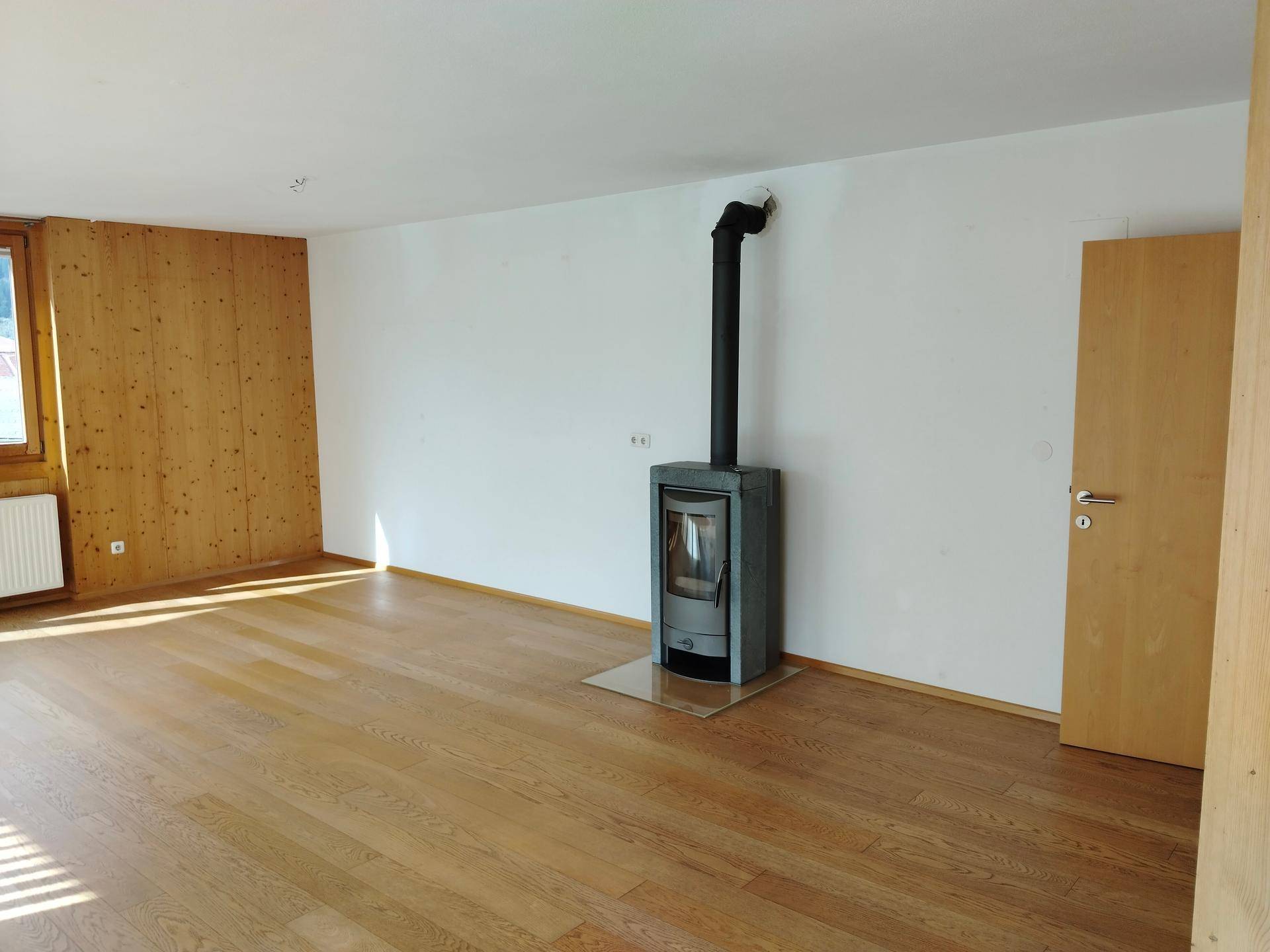 Gemütliches Wohnzimmer mit Holzboden, Holzwand und einem modernen Holzofen.