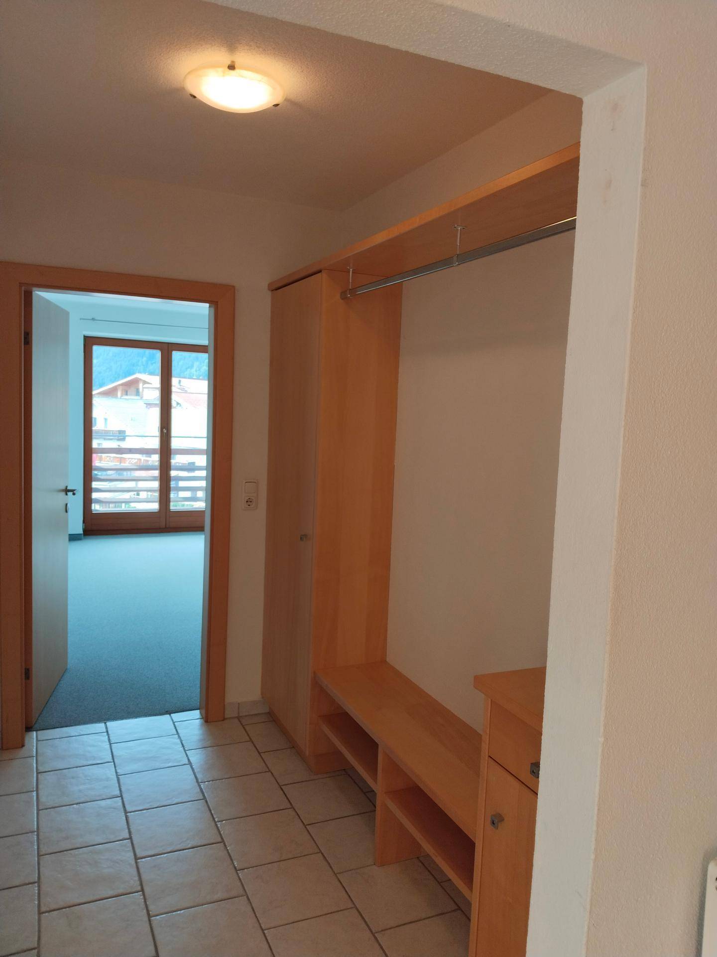 Eingangsbereich mit praktischer Garderobe und Fliesenboden, führt zu einem Zimmer mit Balkon.