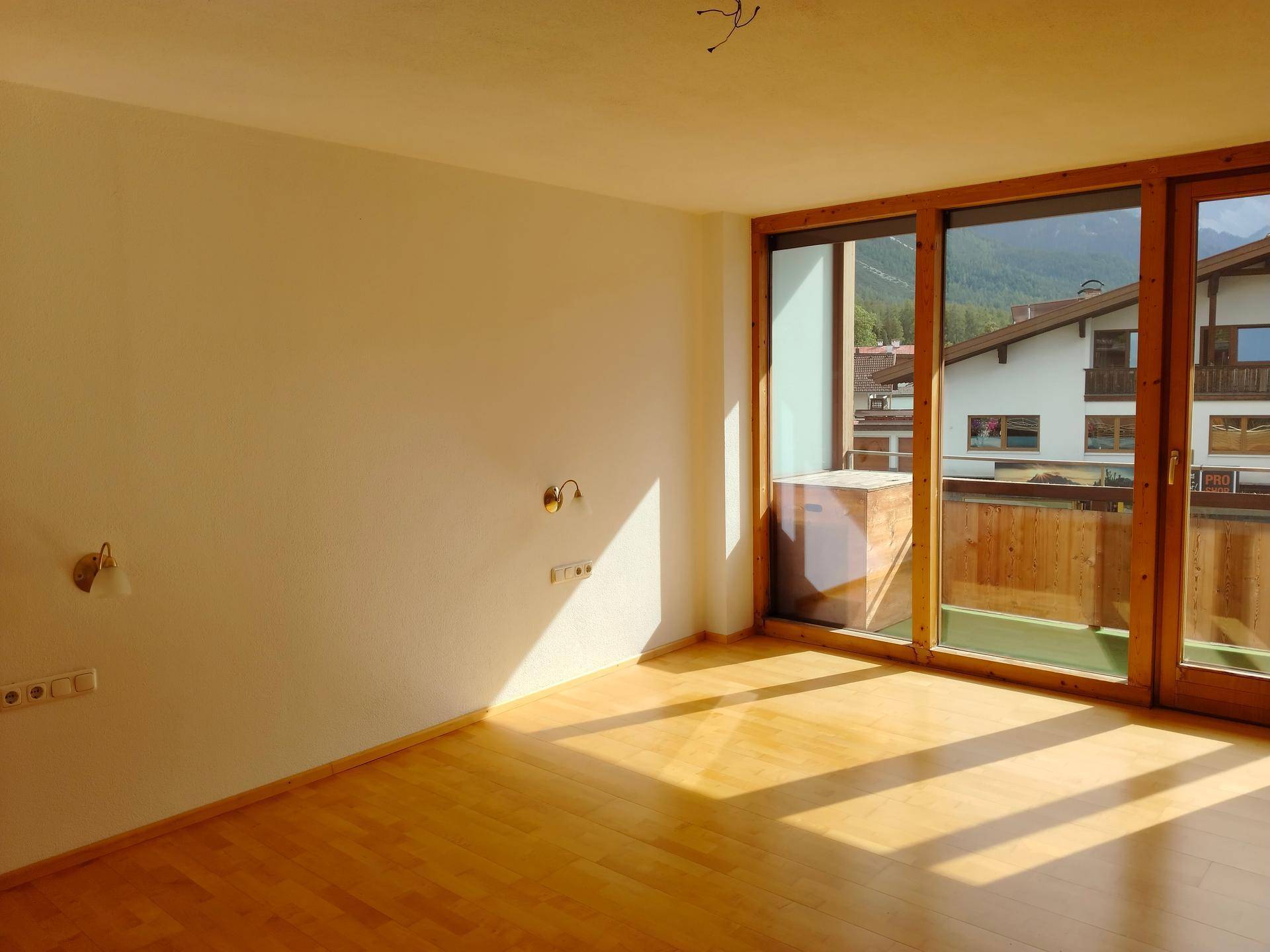 Helles Zimmer mit Holzboden, großen Fenstern und Zugang zu einem Balkon mit Bergblick.
