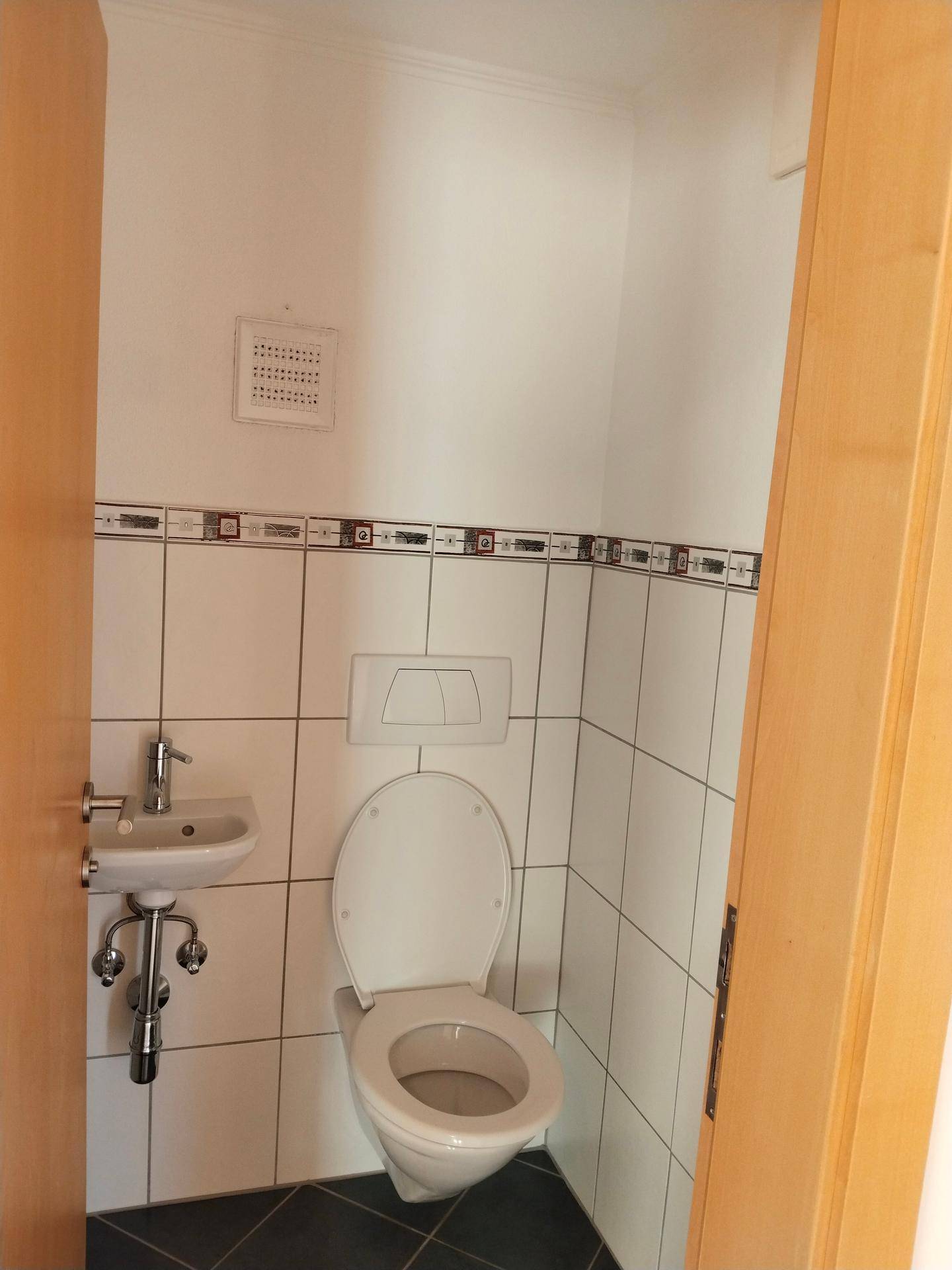 Separates WC mit Wand-WC und kleinem Handwaschbecken, gefliest.