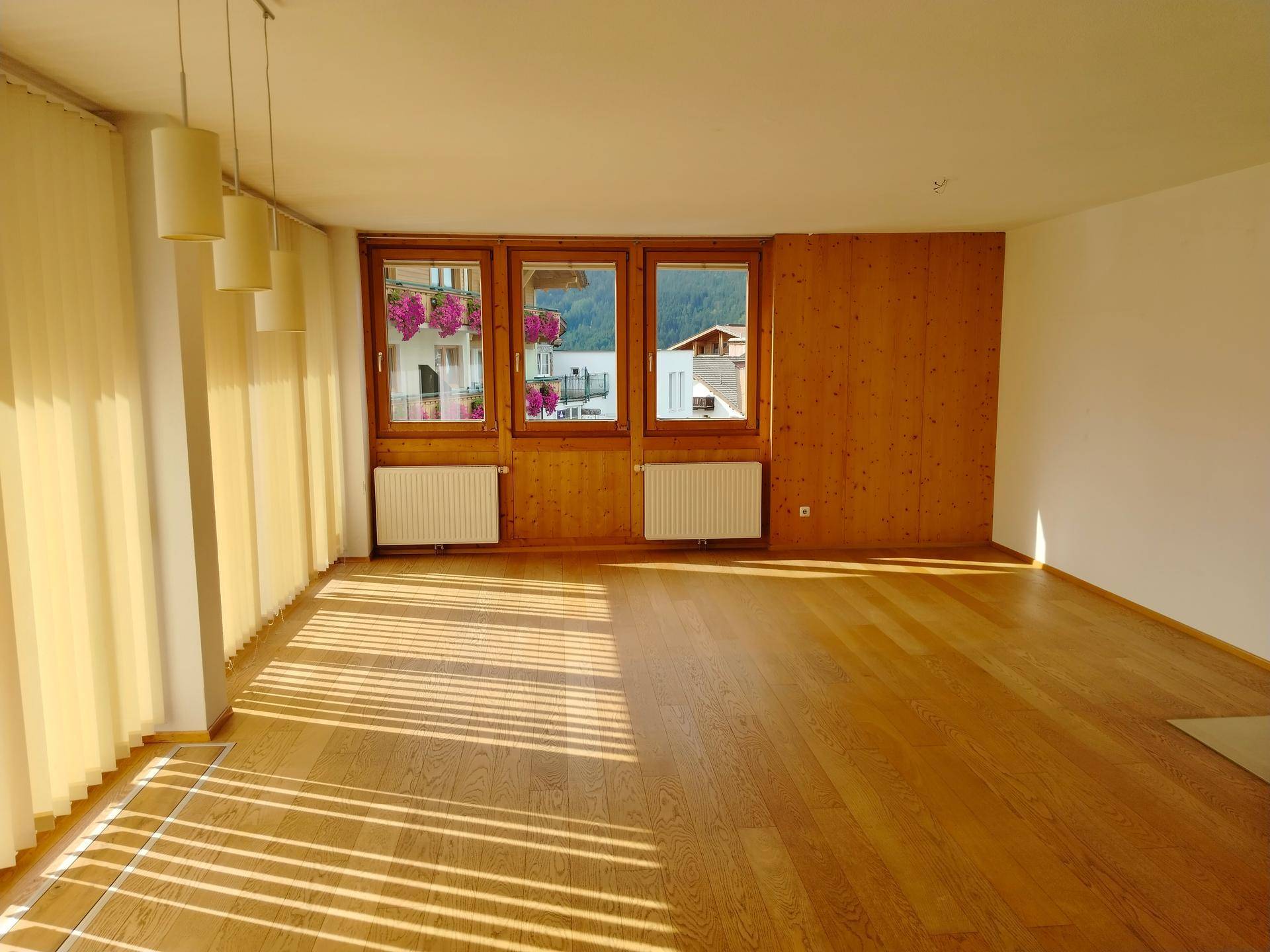 Geräumiges Wohnzimmer mit Holzboden, Holzwand und Fenstern mit Blick auf die Berge.