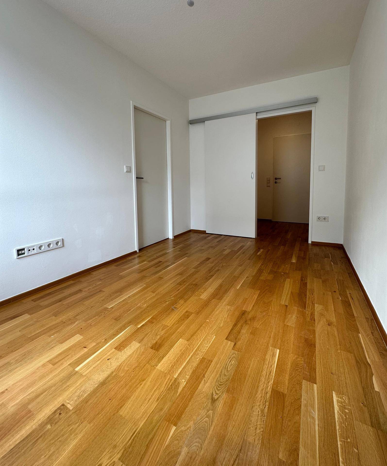 Heller Raum mit Holzboden und Schiebetür, der vielseitig genutzt werden kann.