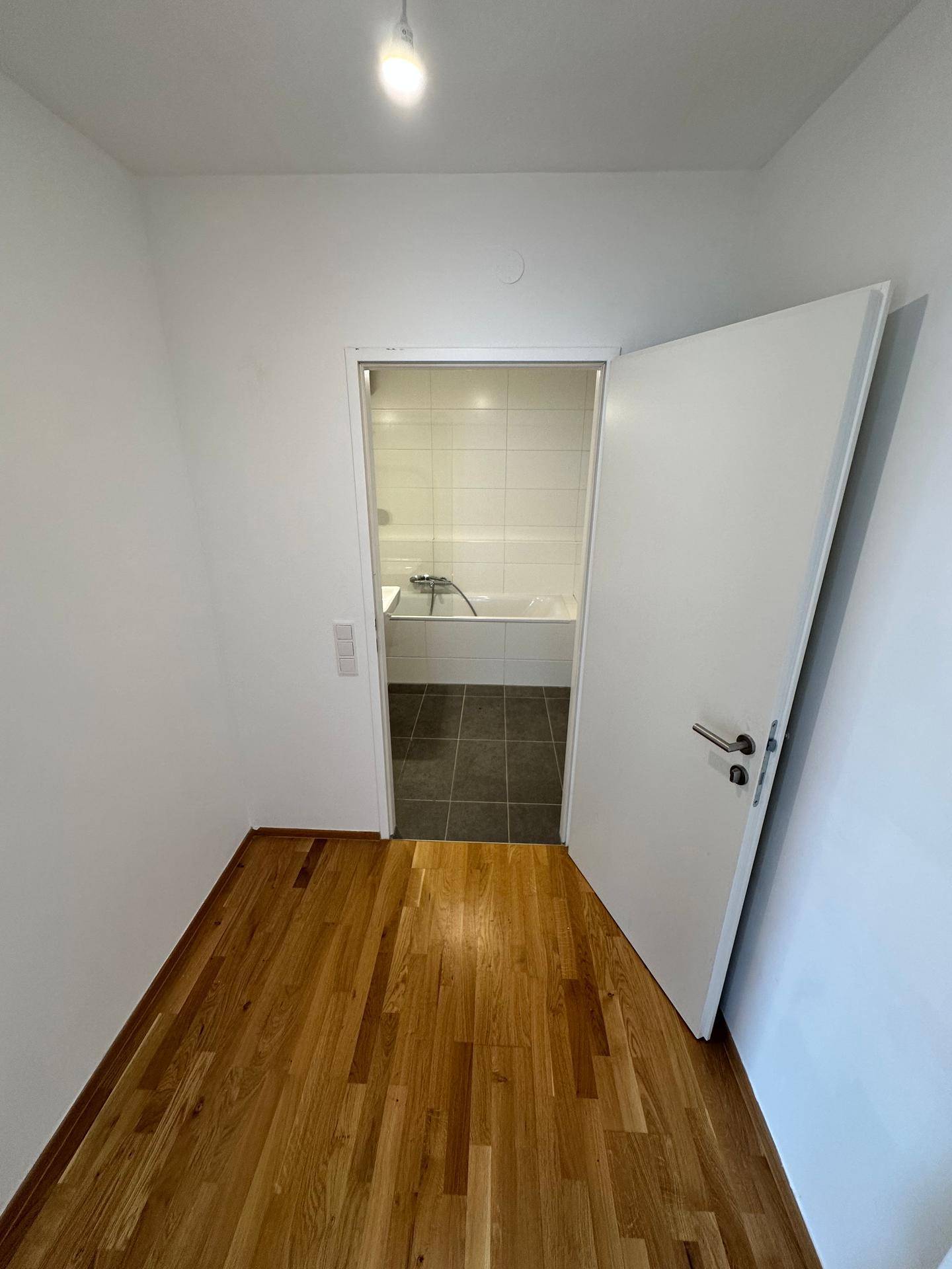 Blick von einem Raum mit Holzboden in ein Badezimmer mit Badewanne und Fliesen.