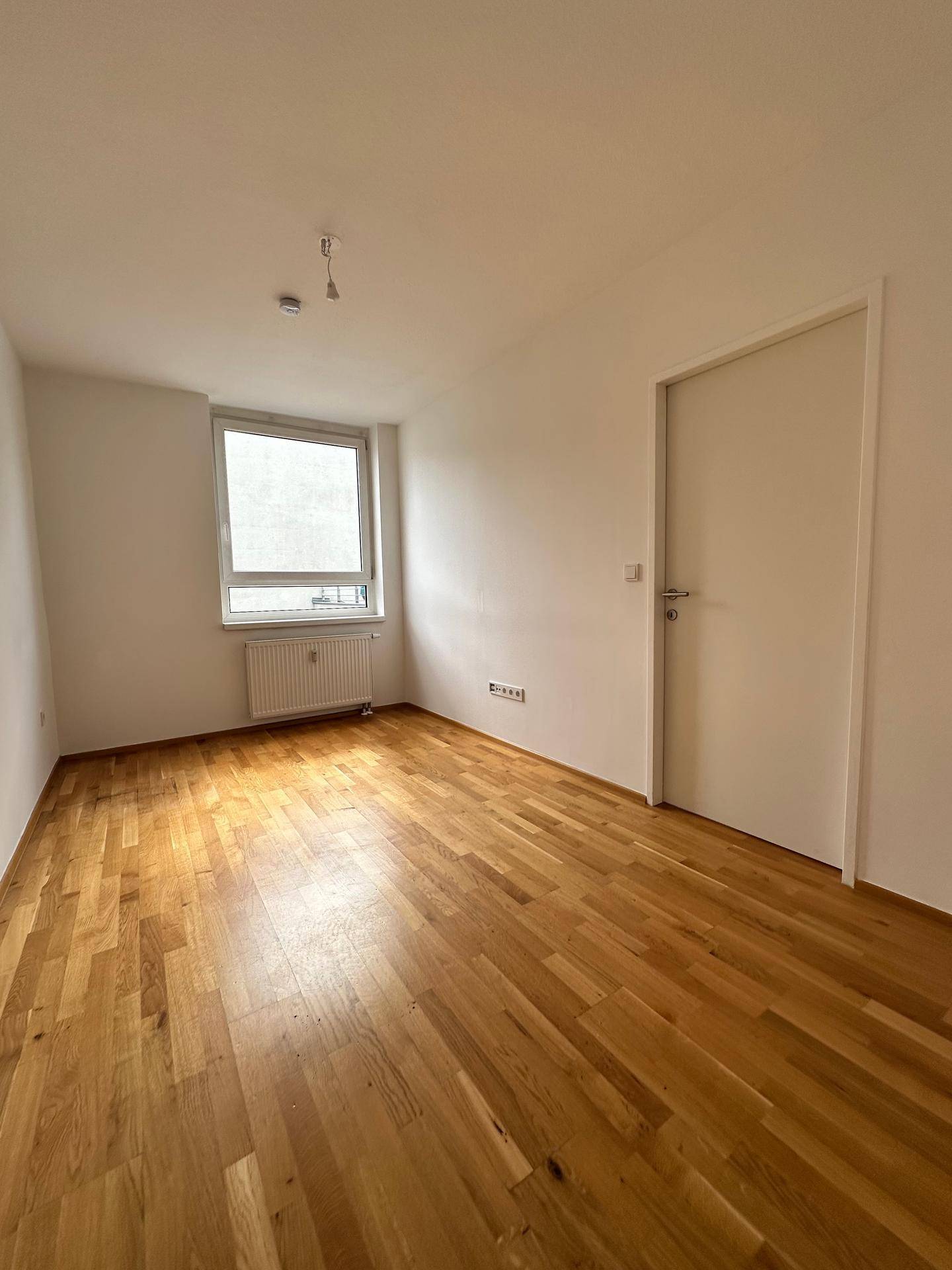 Helles Schlafzimmer mit Parkettboden, weiß gestrichenen Wänden und einem Fenster.