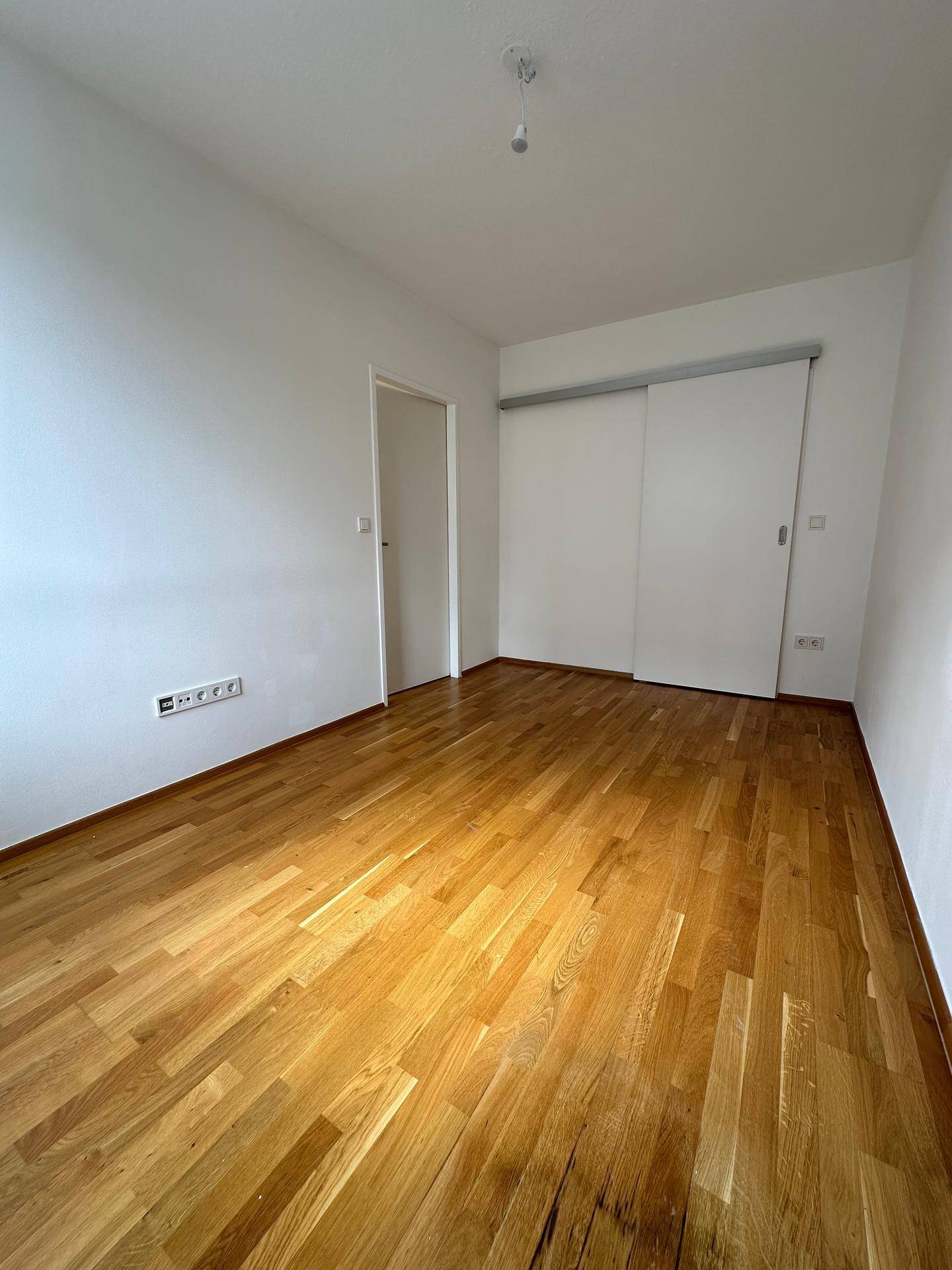 Geräumiges Zimmer mit Parkettboden und einer praktischen Schiebetür zu einem weiteren Bereich.