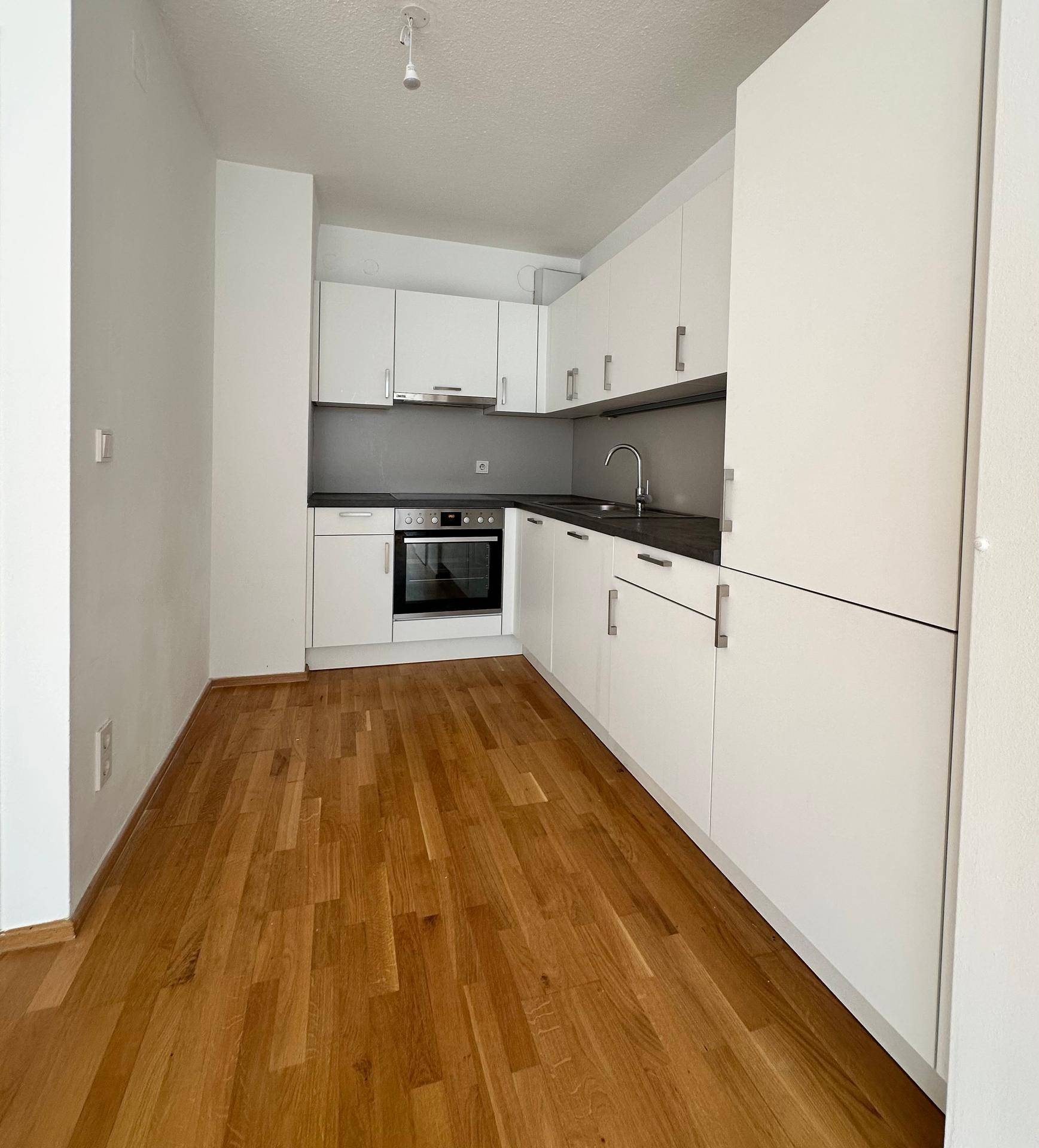 Moderne Einbauküche mit weißen Schränken, dunkler Arbeitsplatte und integriertem Backofen.