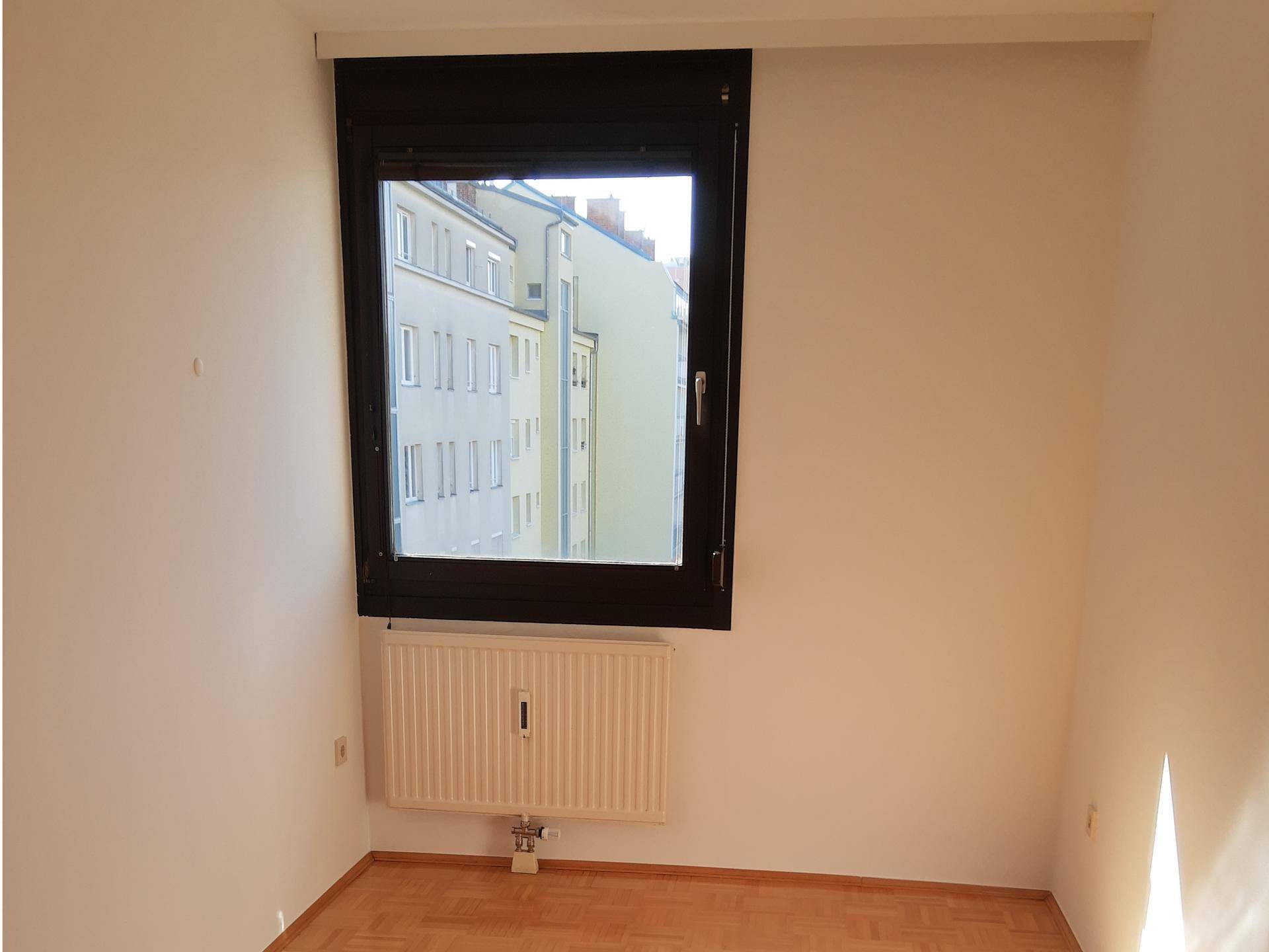 Weiteres helles Zimmer mit Parkettboden und einem Fenster, das einen Blick auf die Stadt bietet.