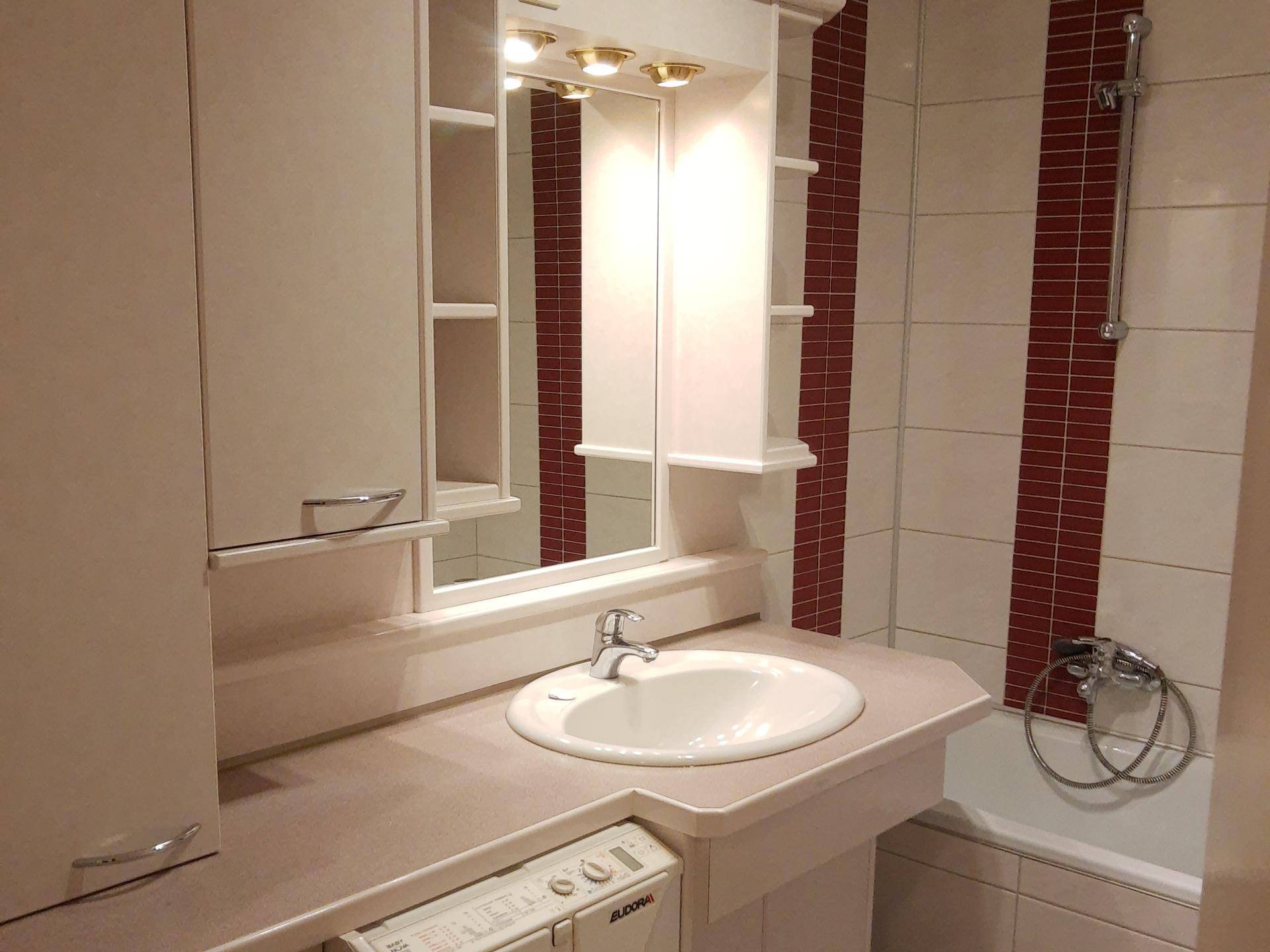 Badezimmer mit Waschbecken, Spiegelschrank, Badewanne und roten Akzentfliesen.