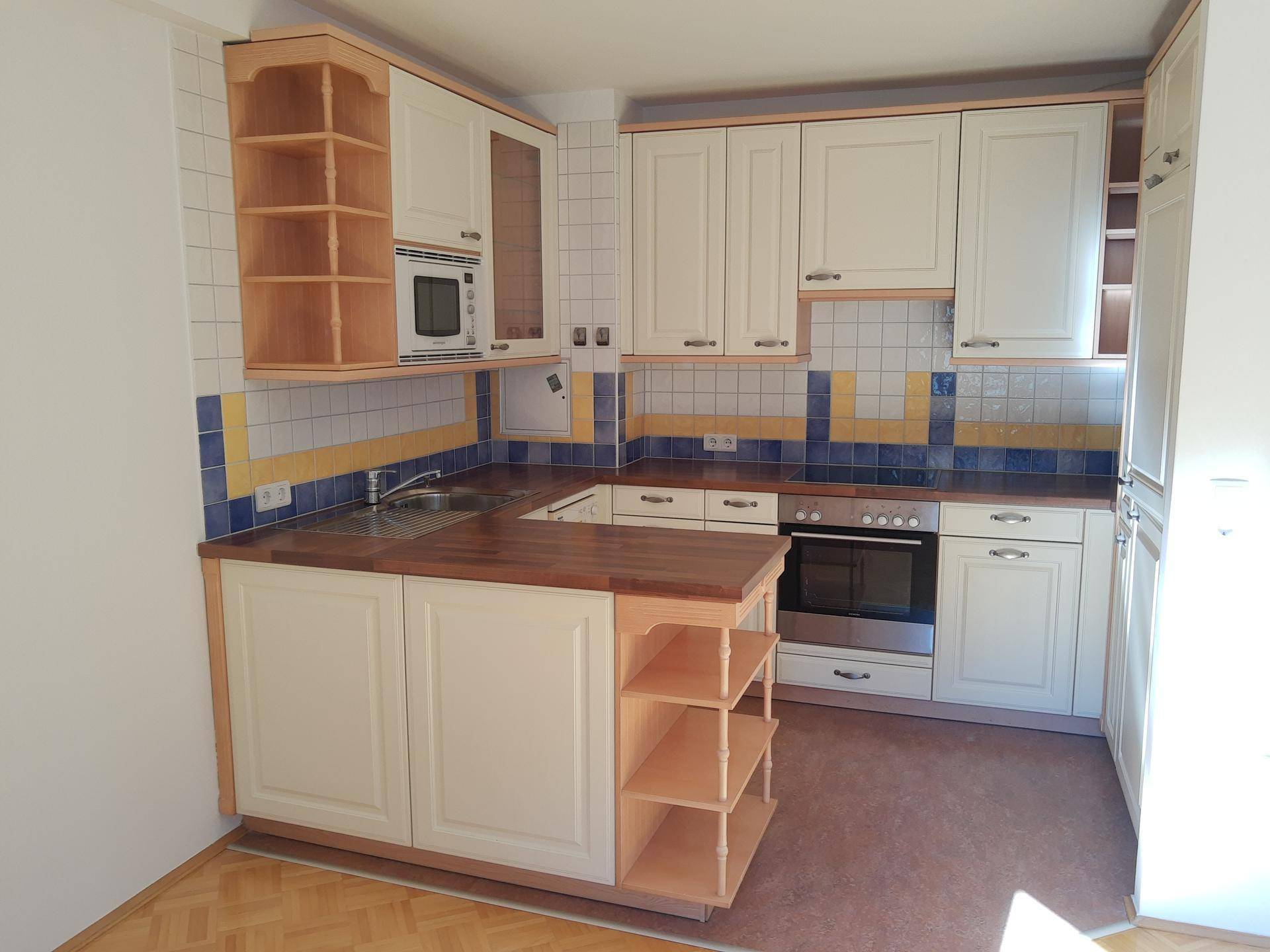 Helle Küche mit weißen Schränken, Holztheke und blauen Akzentfliesen, ausgestattet mit modernen Geräten.