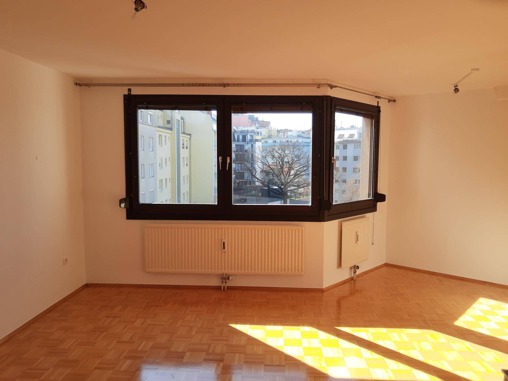 Geräumiges Wohnzimmer mit Parkettboden und einem Erkerfenster mit Blick auf die Stadt.