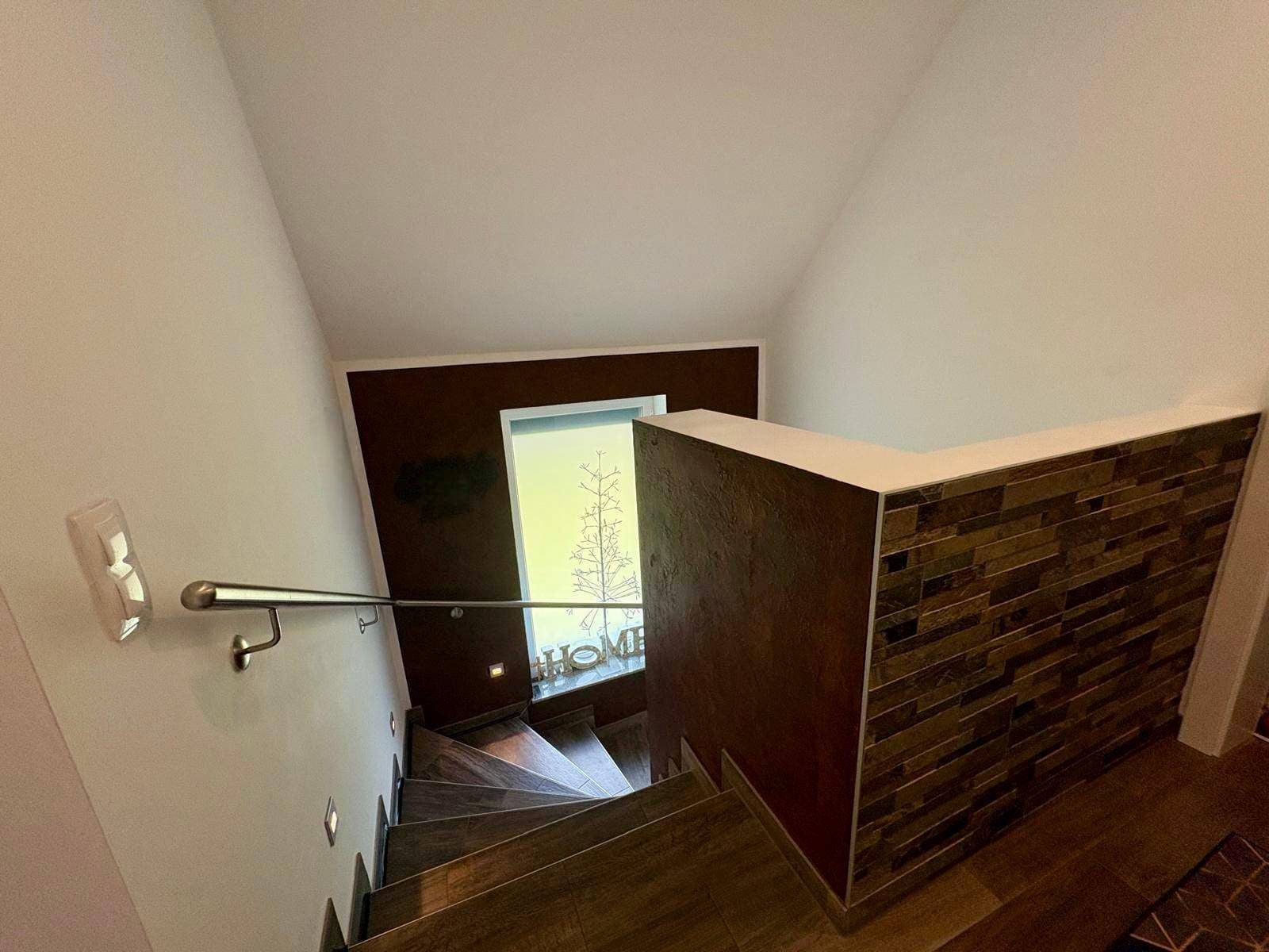 Treppenaufgang von oben gesehen mit Holzstufen, Edelstahlgeländer und Fenster.