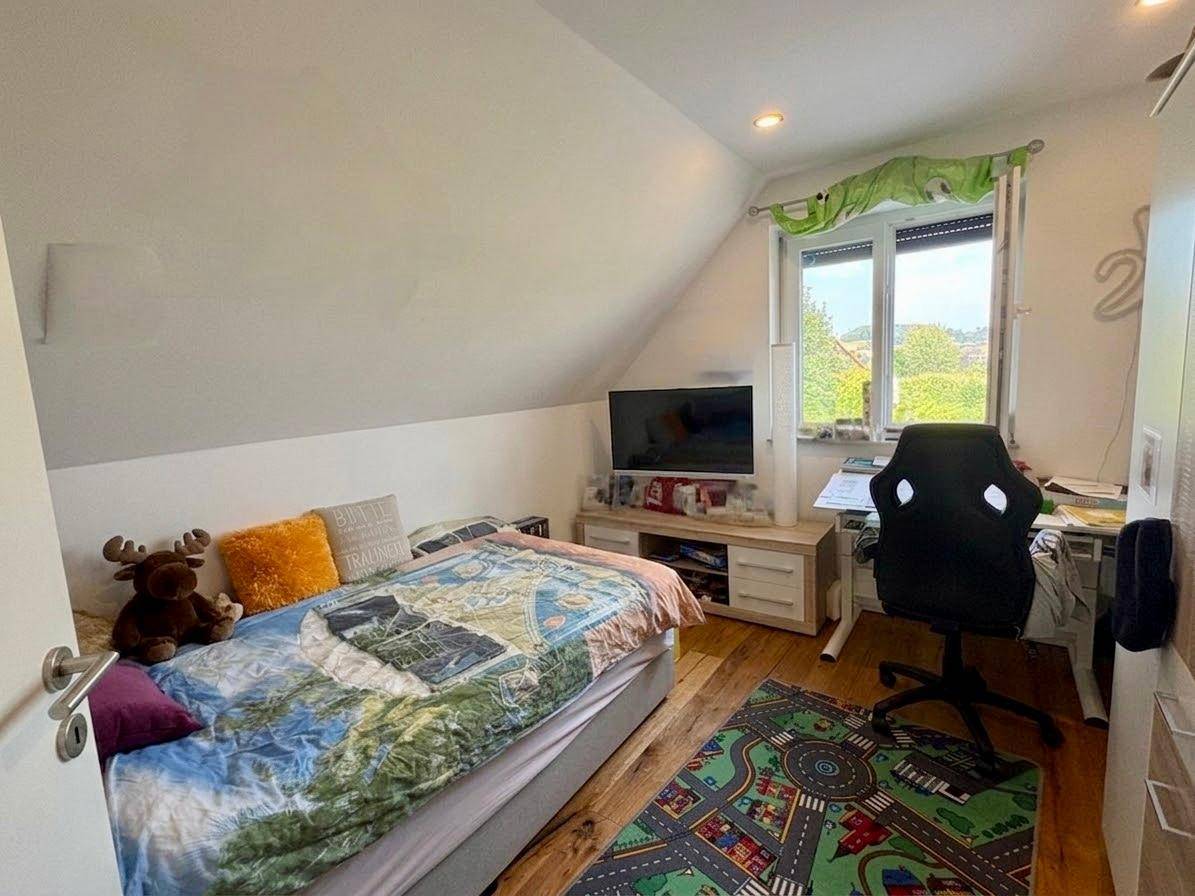 Kinderzimmer mit Einzelbett, Schreibtisch und Holzboden unter der Dachschräge.